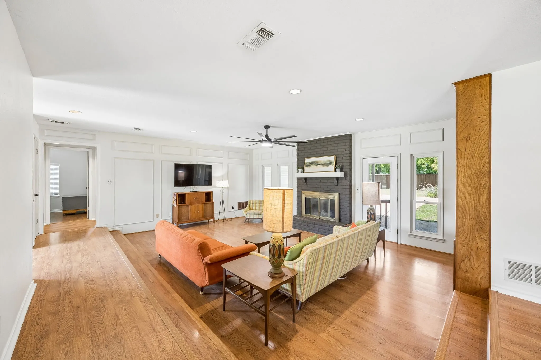 Spacious living area featuring wood-finish flooring, a painted brick fireplace, and built-in wall paneling