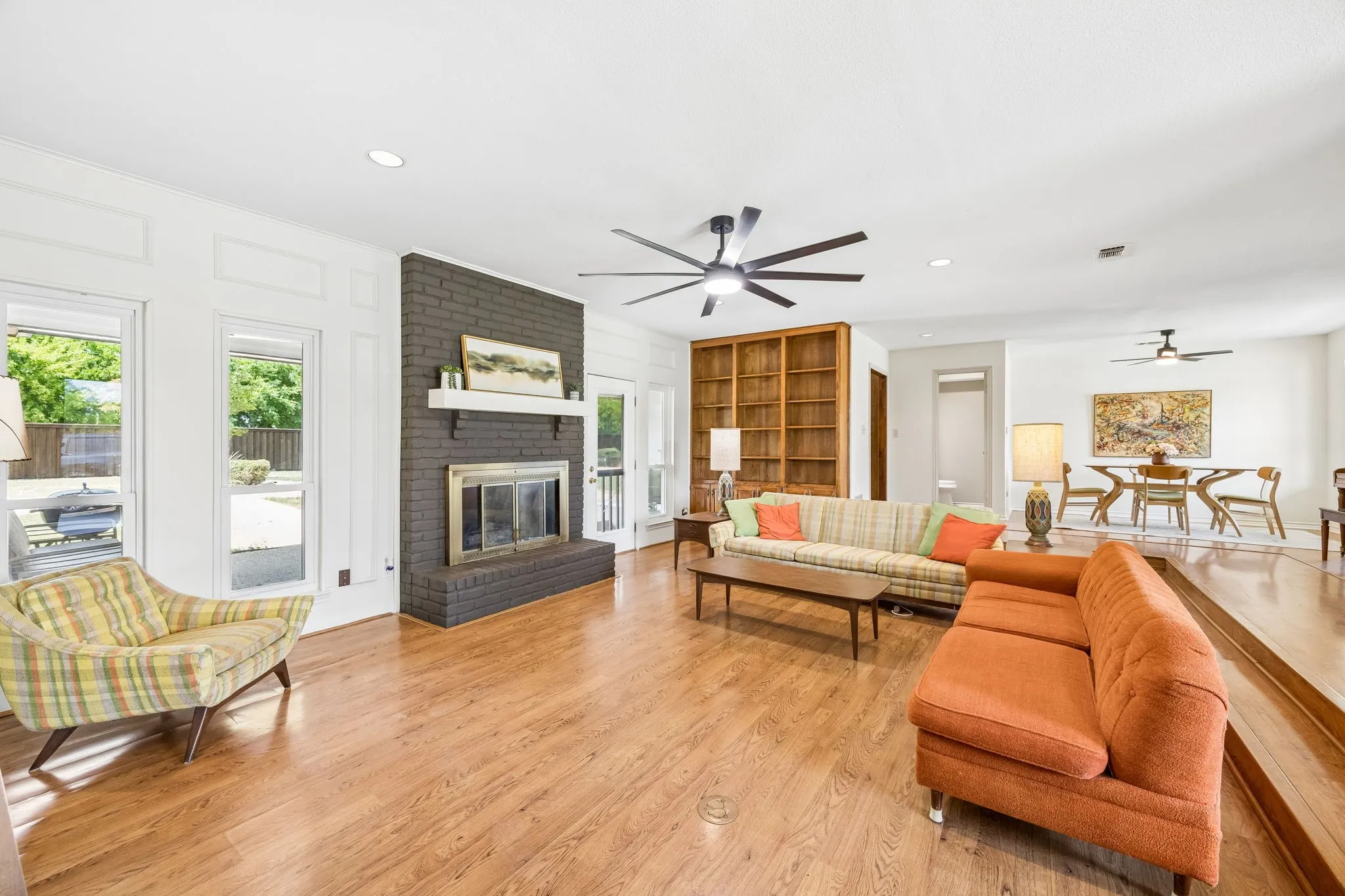 Spacious living area featuring wood-finish flooring, a painted brick fireplace with a mantel, and multiple large windows