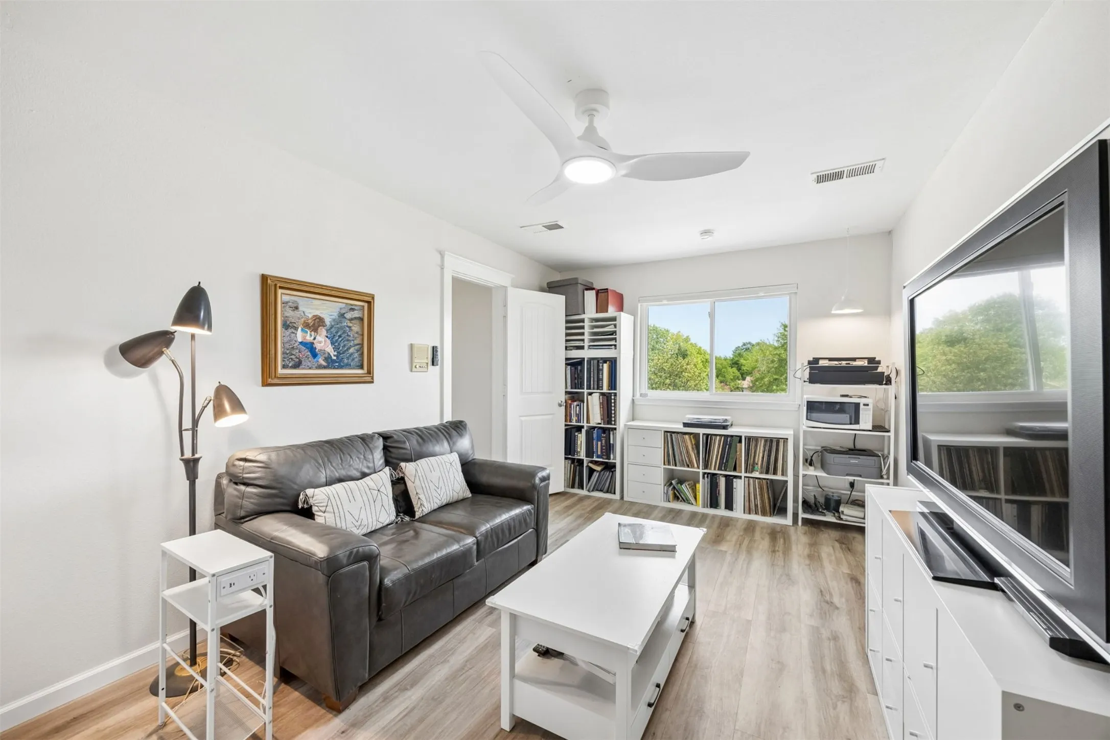 Living area featuring wood-finish flooring, a contemporary ceiling fan with integrated lighting, and multiple windows providing natural illumination