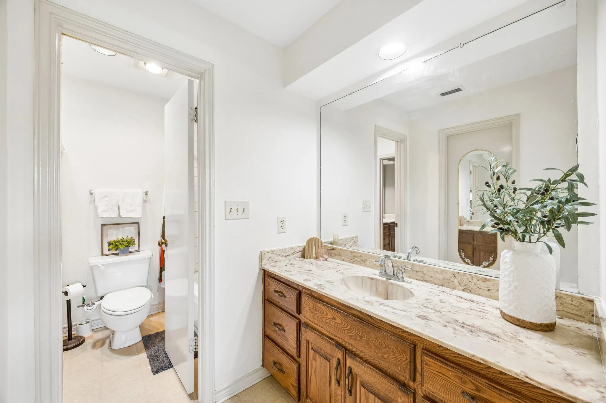 Bathroom vanity with a light-toned stone countertop, integrated sink, and an expansive wall-mounted mirror