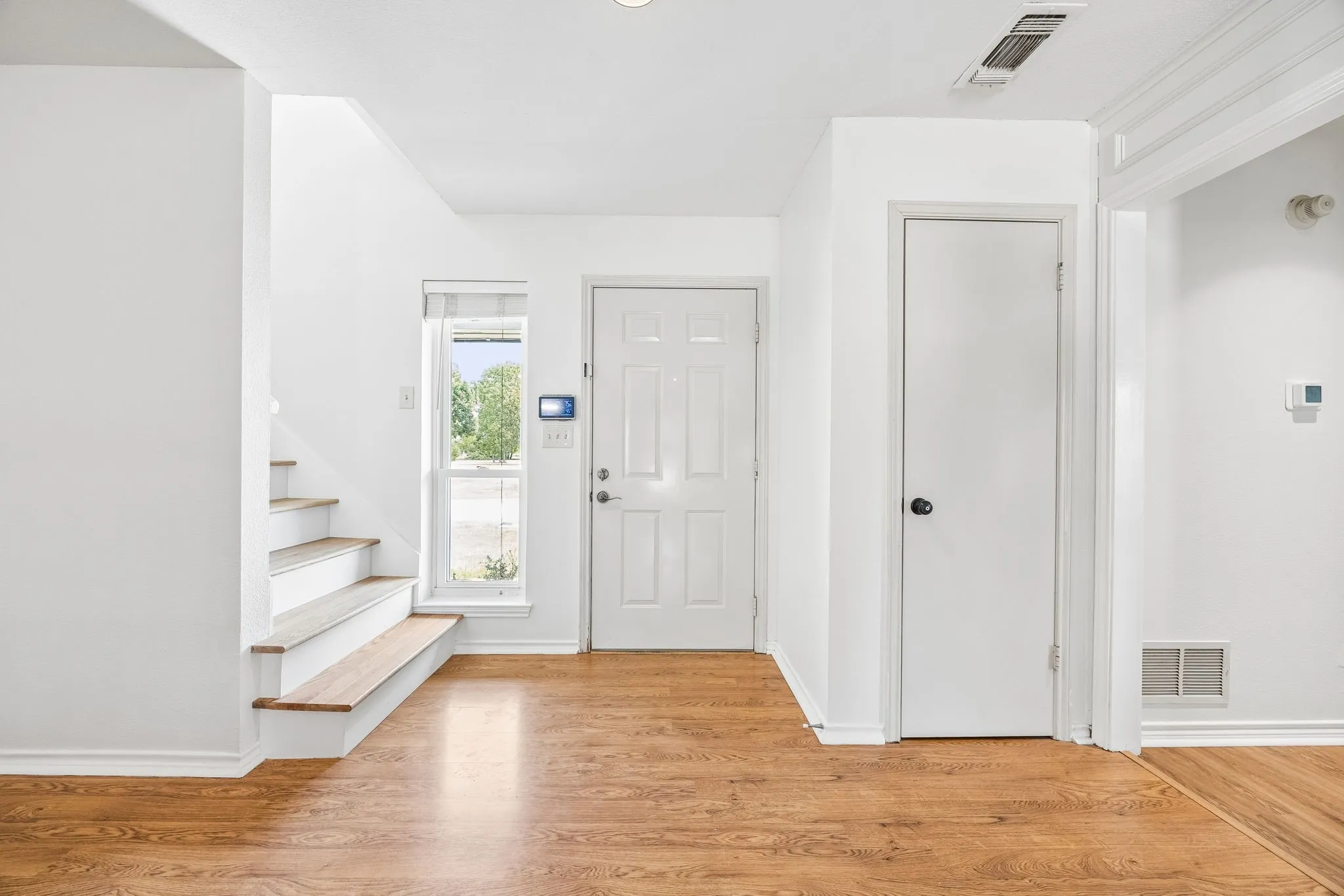 Foyer featuring wood-finish flooring, white paneled doors, and a staircase with wood treads