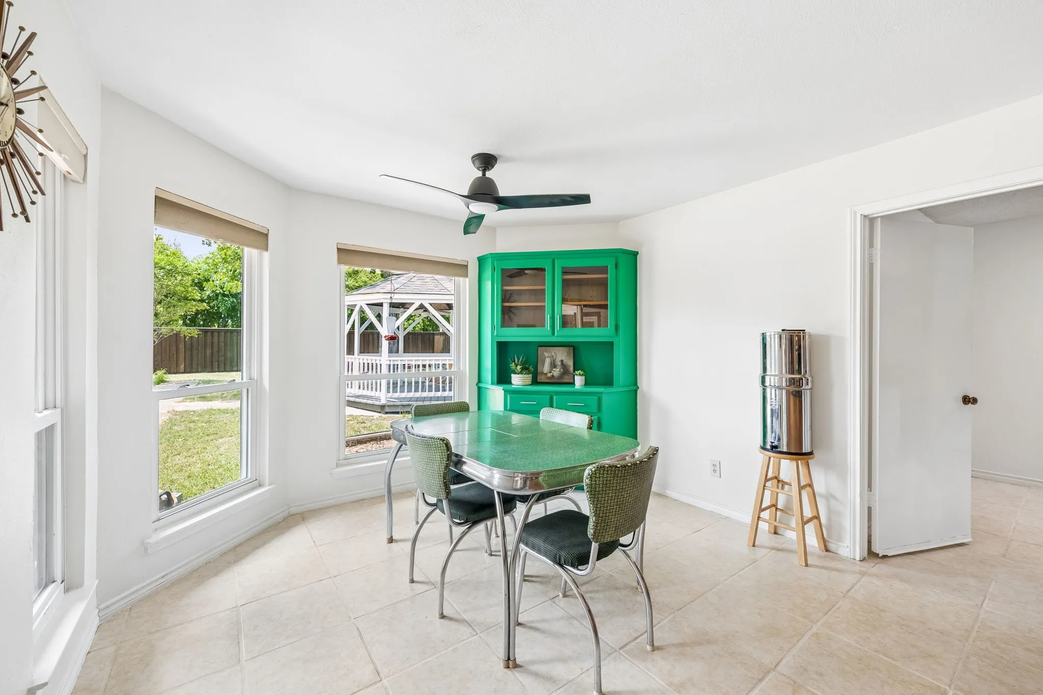Light-filled dining area featuring multiple windows, a ceiling fan, and a built-in corner hutch with glass-front cabinetry