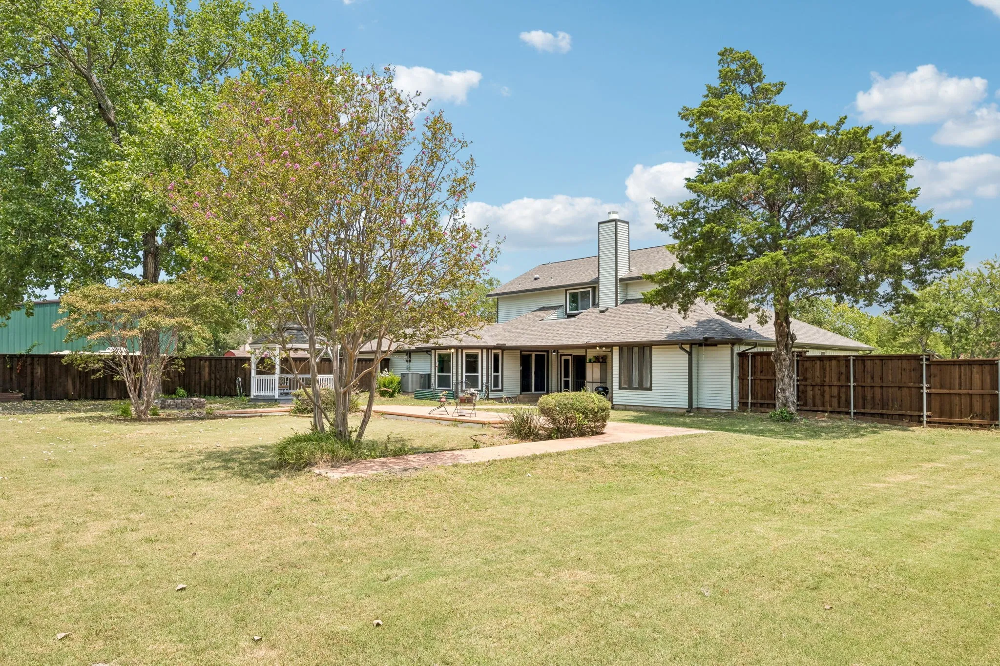 Expansive backyard featuring a manicured lawn, established trees, and a privacy fence