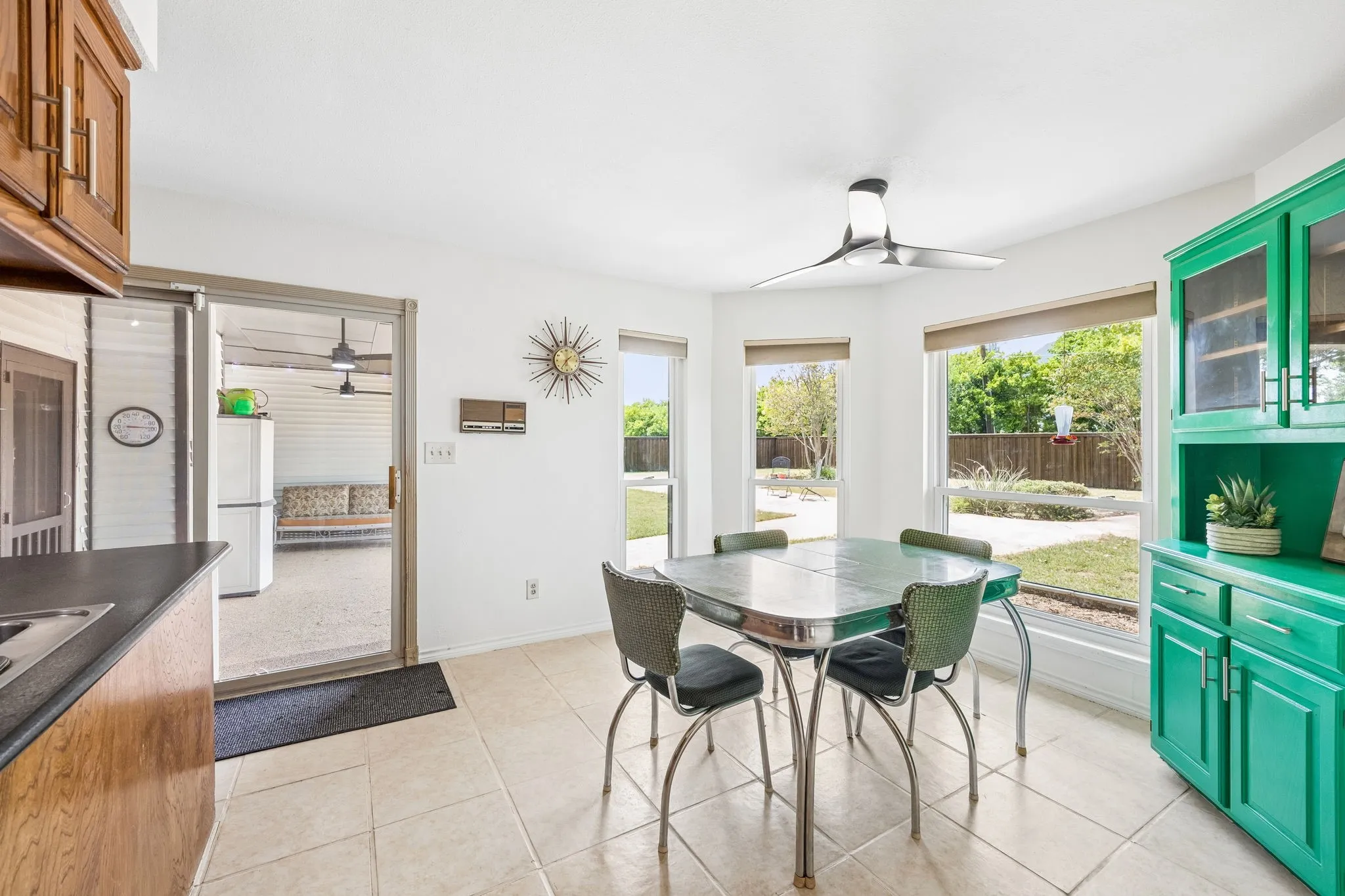 Bright dining area featuring tile flooring, a contemporary ceiling fan, and multiple windows overlooking the backyard