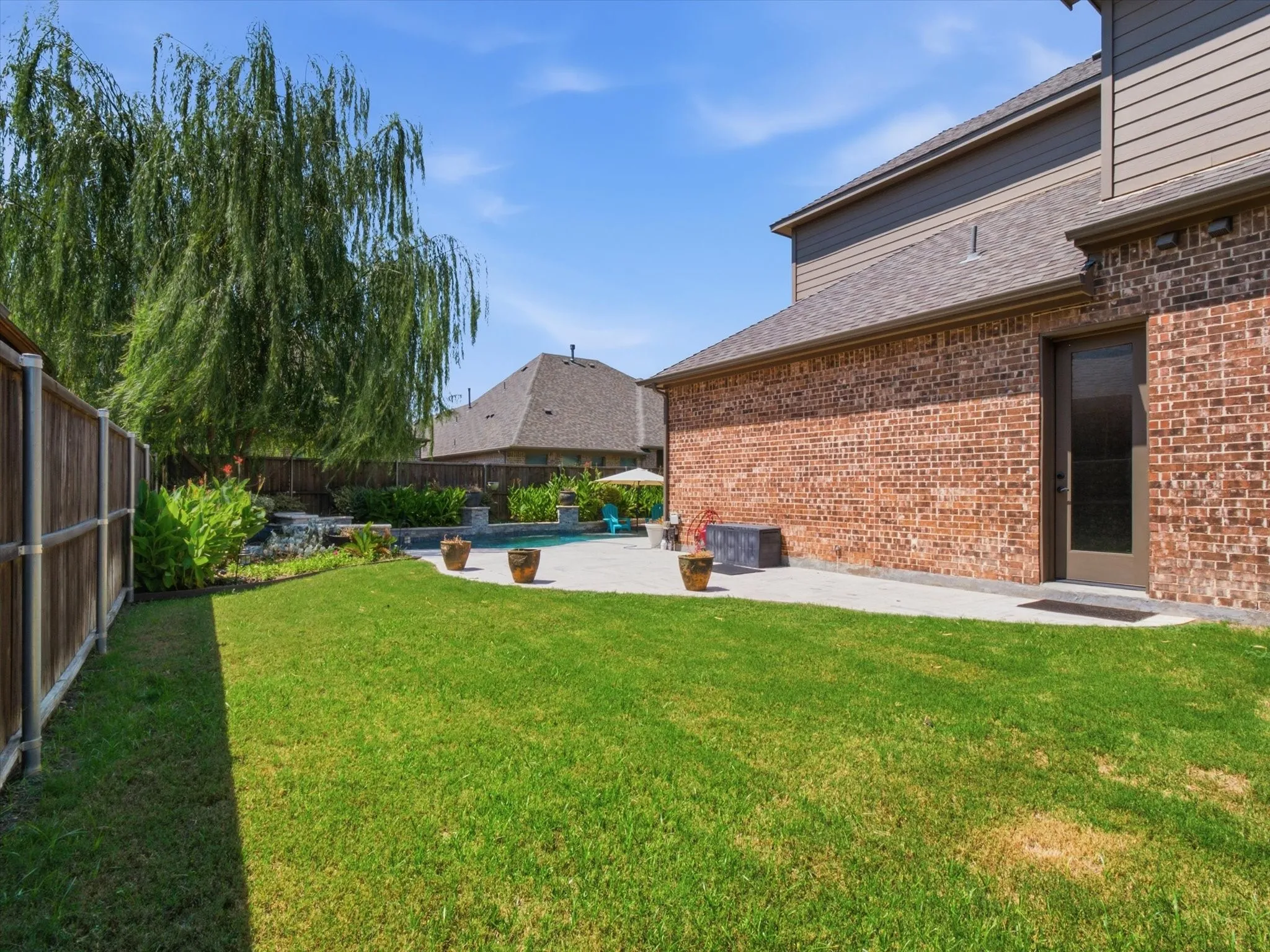 Spacious backyard retreat featuring a manicured lawn, mature weeping willow, wooden privacy fencing, and a brick exterior with direct patio access