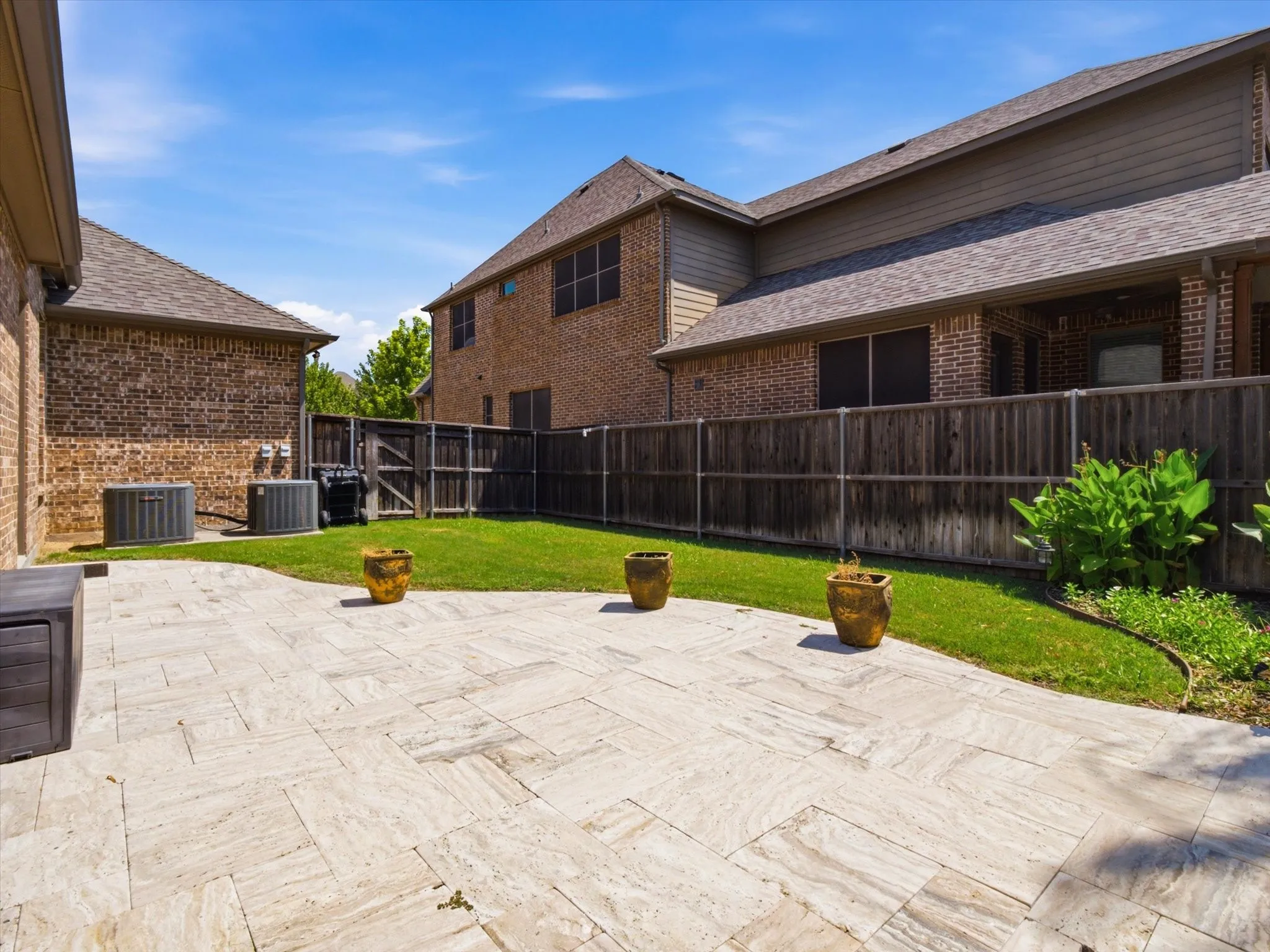 Expansive paver patio with clean linear design, anchored by mature landscaping and decorative planters