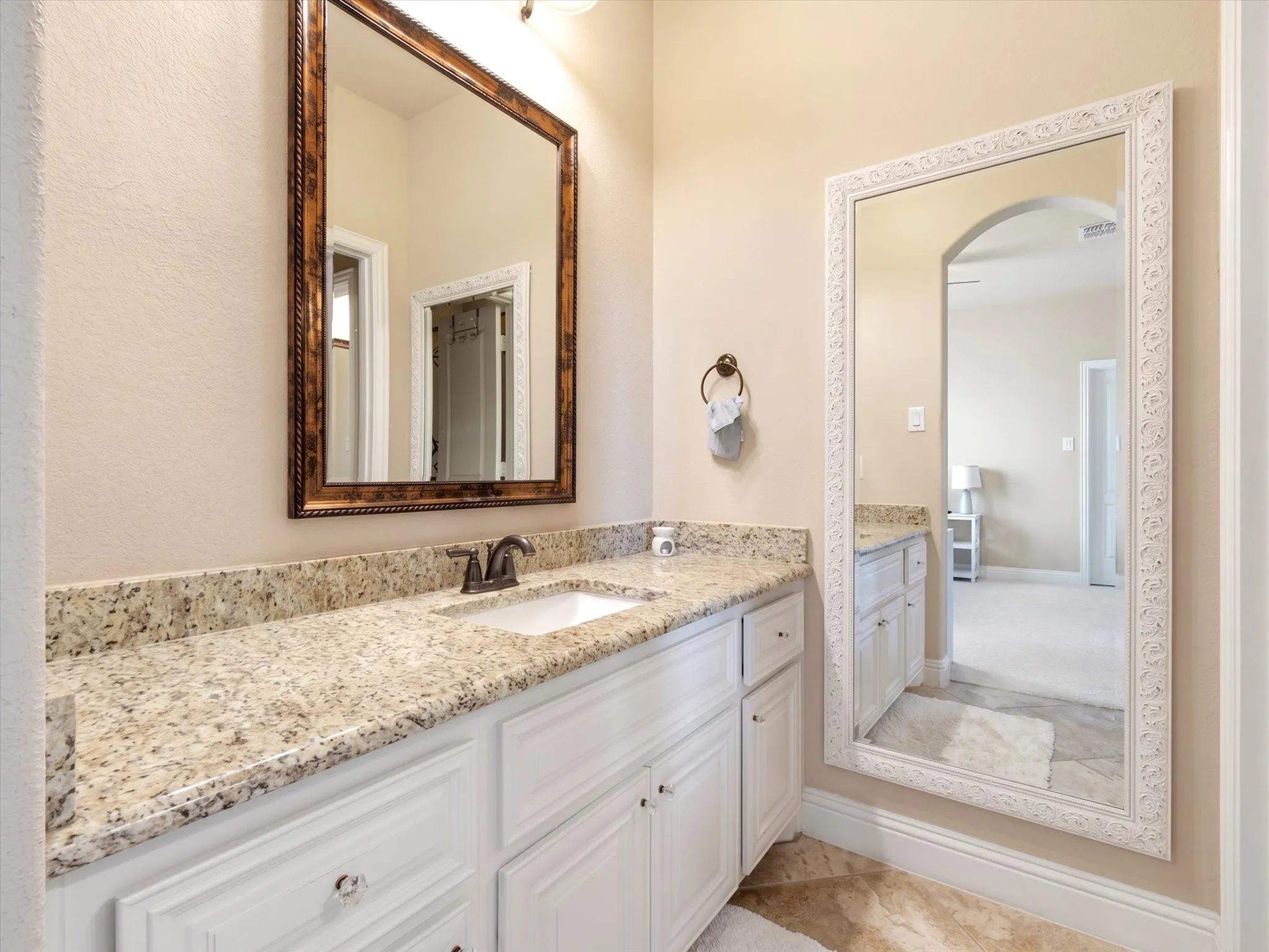 Bathroom vanity featuring a light-toned granite countertop with an undermount sink and a bronze-finish faucet
