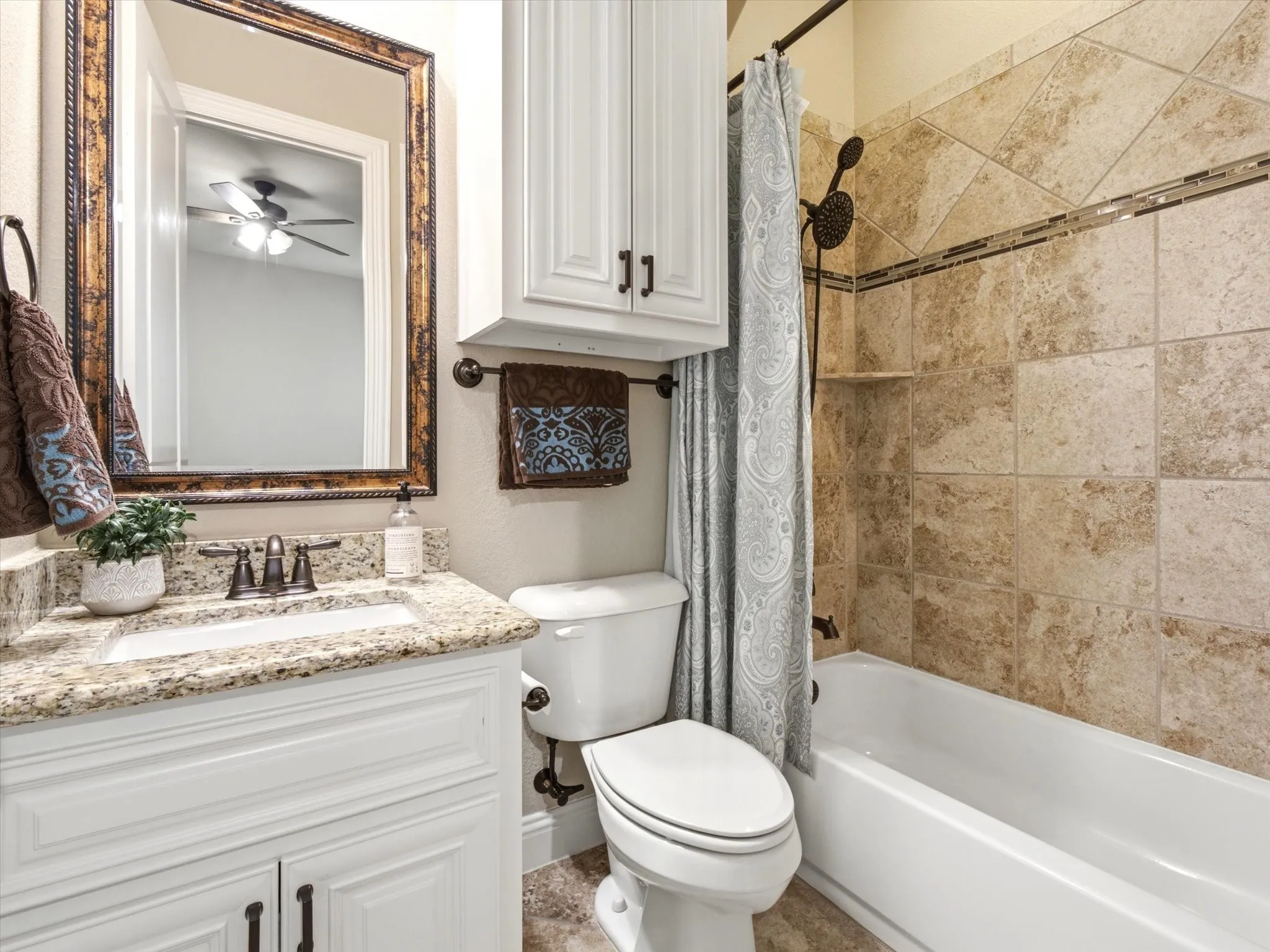 Bathroom featuring a granite countertop vanity with white cabinetry, bronze fixtures, a framed mirror, and a tiled shower/tub combination with a decorative accent band