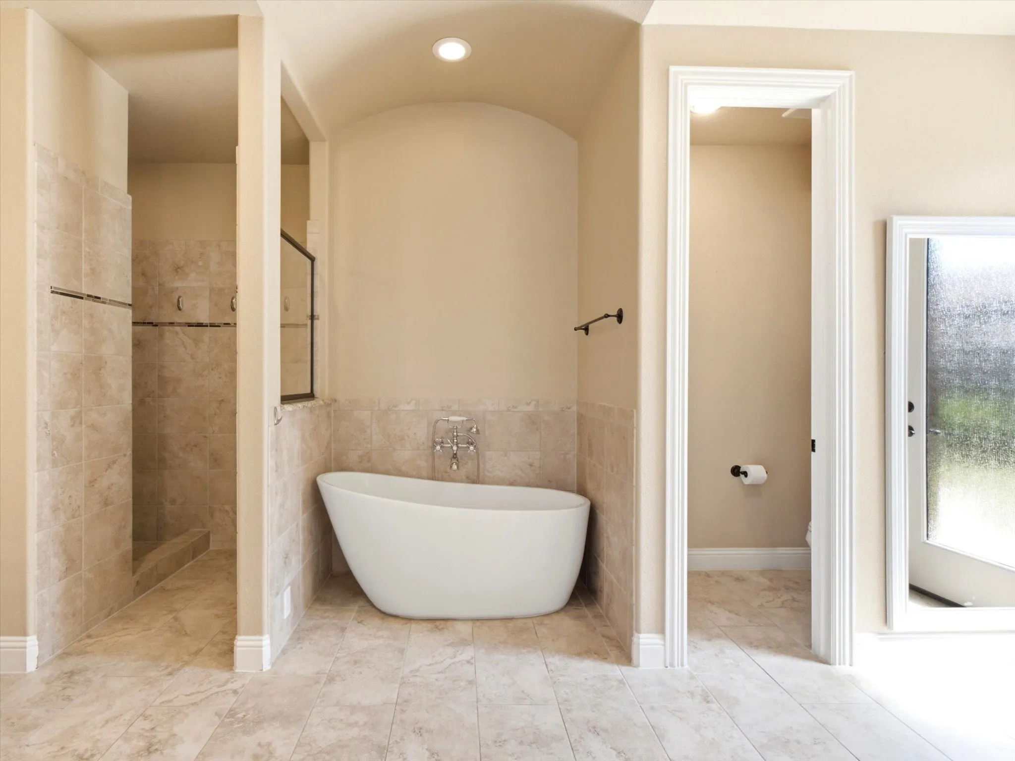 Luxurious primary bathroom suite featuring a freestanding soaking tub, walk-in shower with tile surround and glass enclosure, travertine-look tile flooring, and soft neutral wall finishes