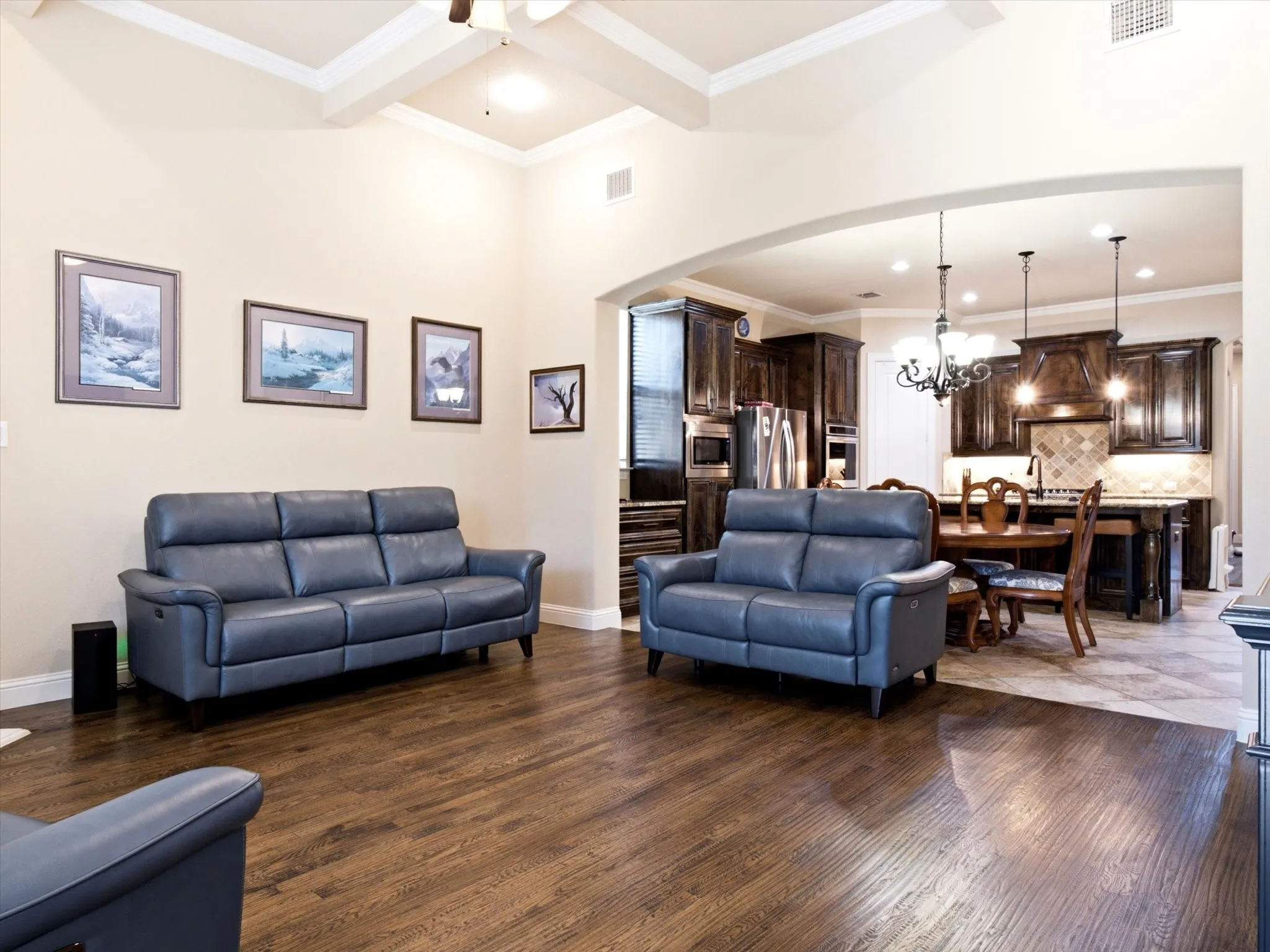 Open-concept living area featuring wood-finish flooring, a vaulted ceiling with exposed beams, and an arched entry to the kitchen