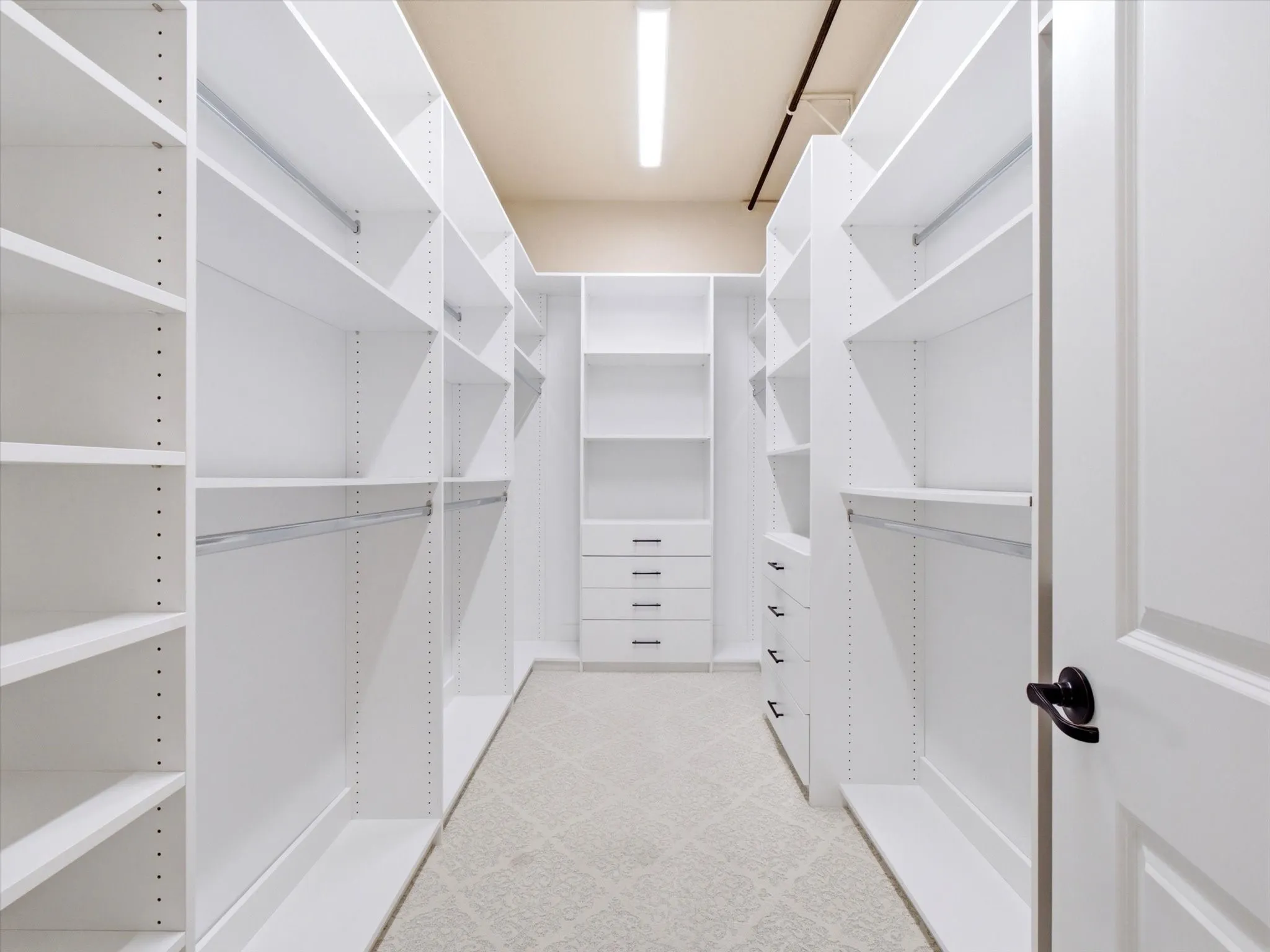 Walk-in closet featuring extensive white built-in shelving, integrated hanging rods, multiple drawer units, and neutral patterned carpeting
