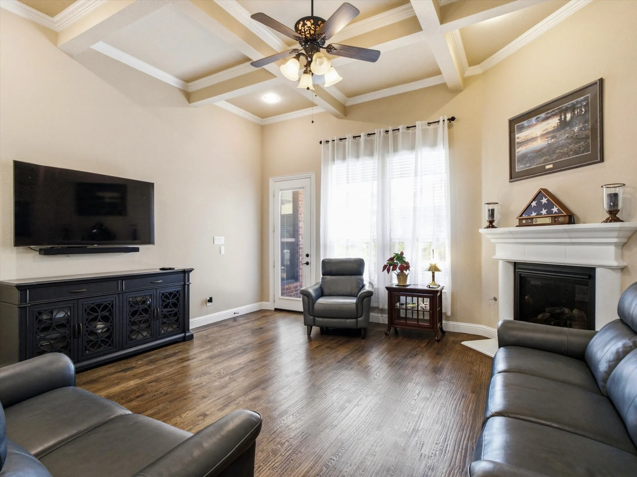Spacious living room featuring coffered ceiling with ceiling fan, wood-finish flooring throughout, and multiple seating areas