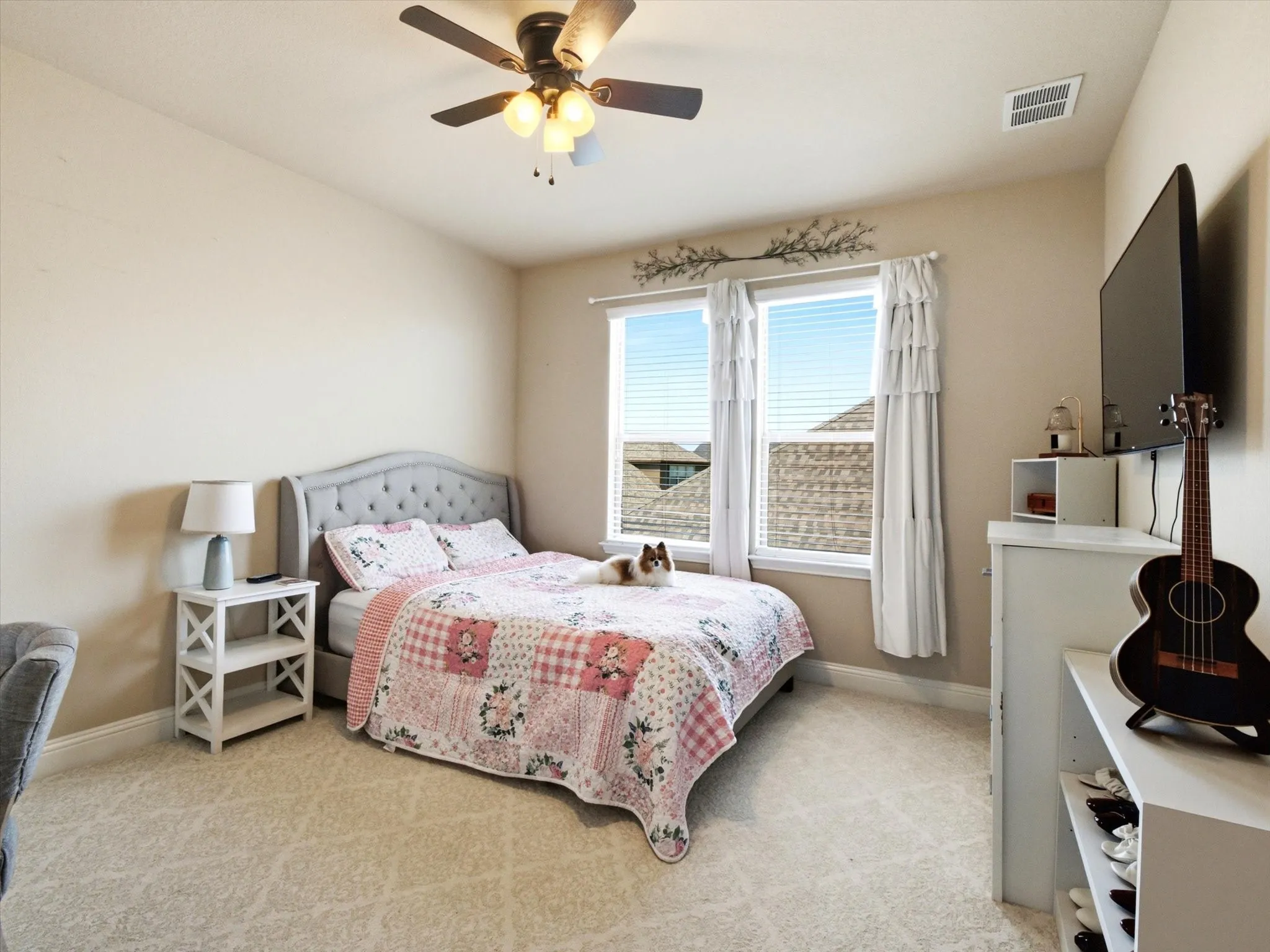 Bedroom featuring a tufted upholstered headboard, ceiling fan with light fixture, carpeted flooring, and a pair of windows with blinds