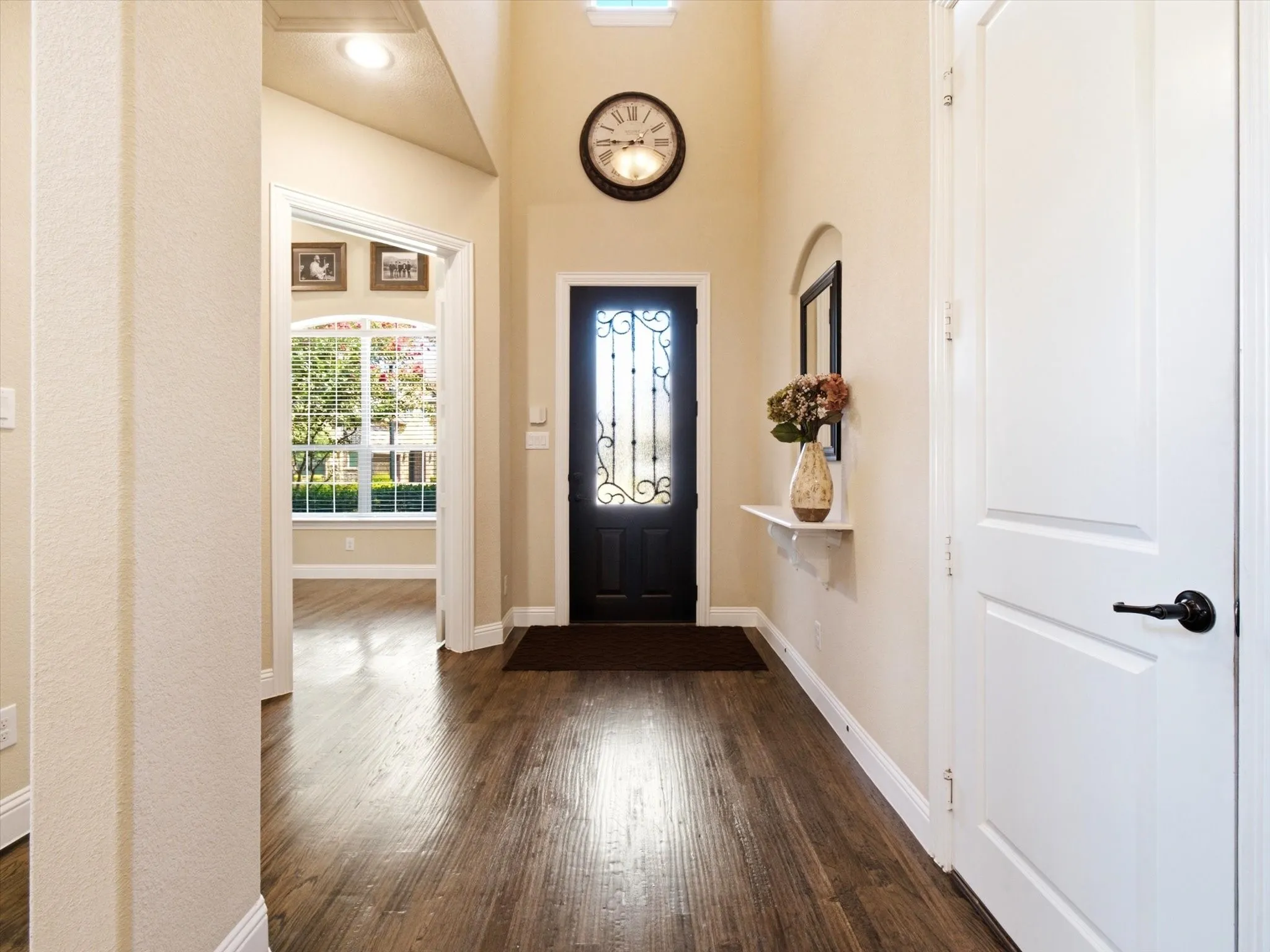Entryway featuring wood-finish flooring, a dark-paneled door with decorative ironwork, and a vaulted ceiling