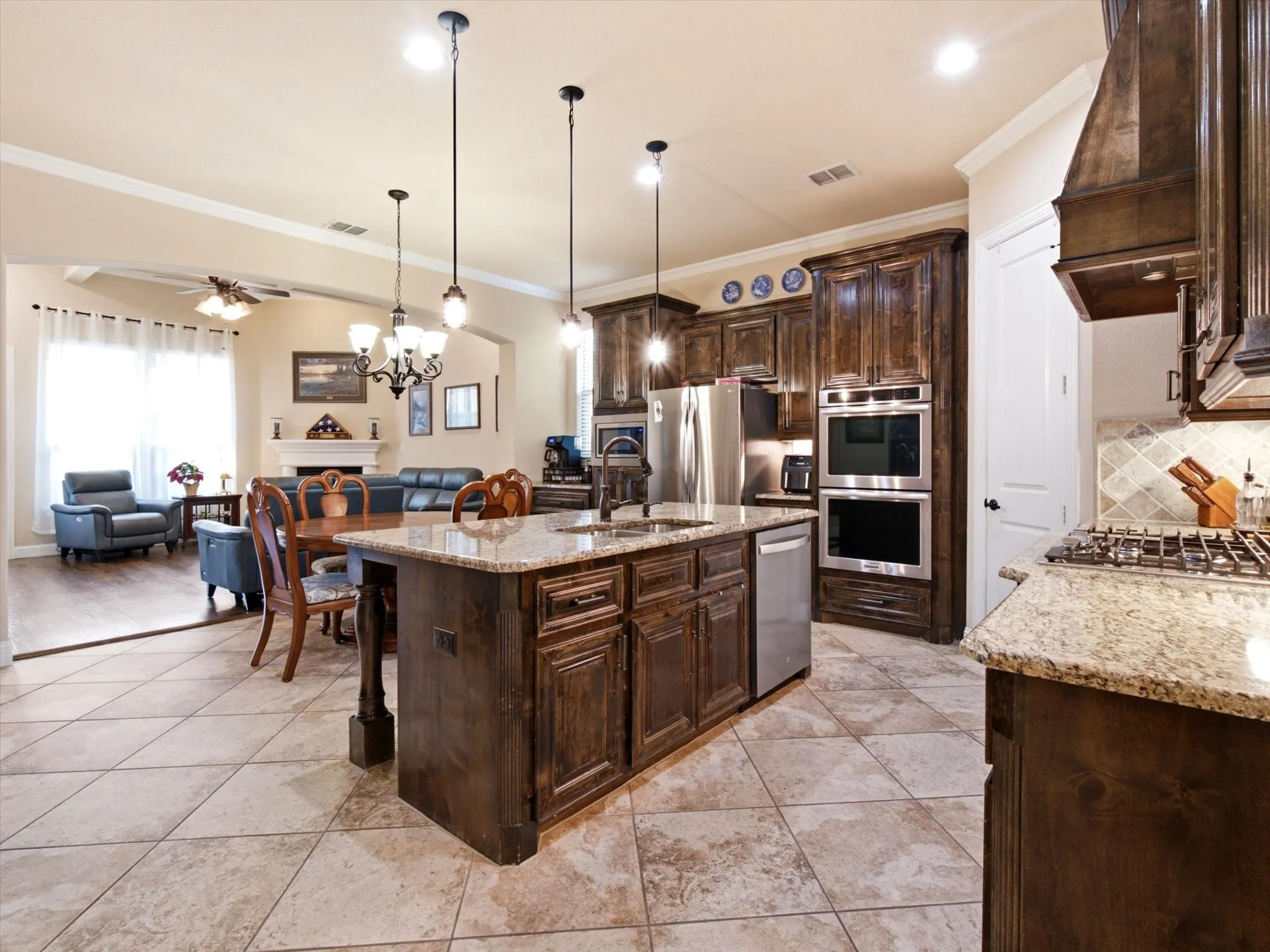 Kitchen featuring an oversized island with a double basin sink, stainless steel appliances including double ovens and a gas range, dark wood cabinetry, and light-toned stone countertops