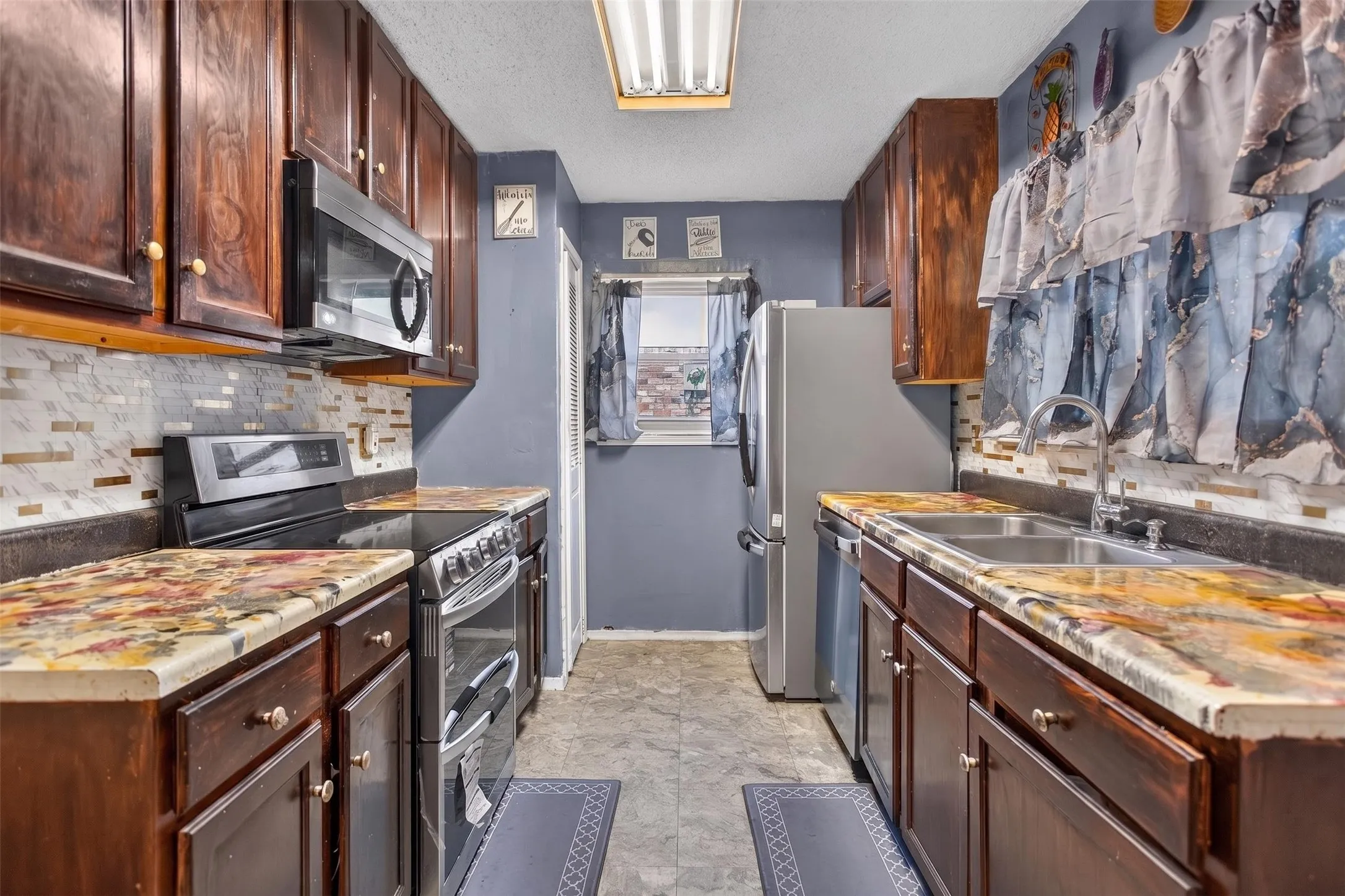 Galley kitchen featuring wood cabinetry, stone countertops, stainless steel appliances, and a mosaic tile backsplash