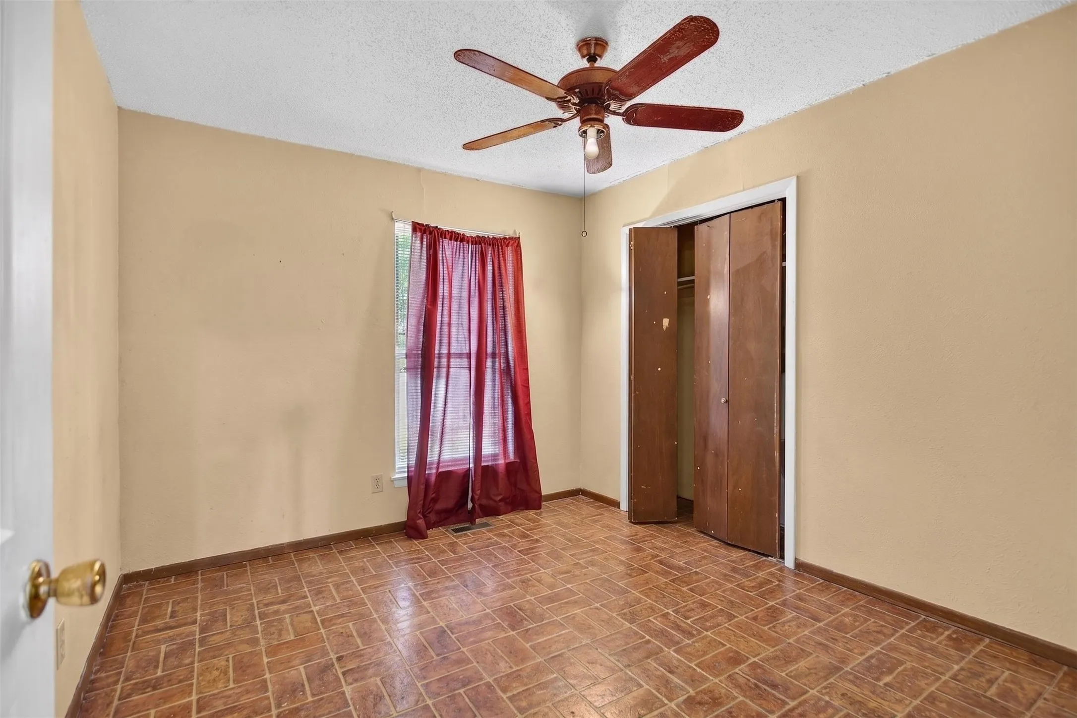 Room featuring textured ceiling, a ceiling fan with integrated lighting, and a window with a sheer curtain