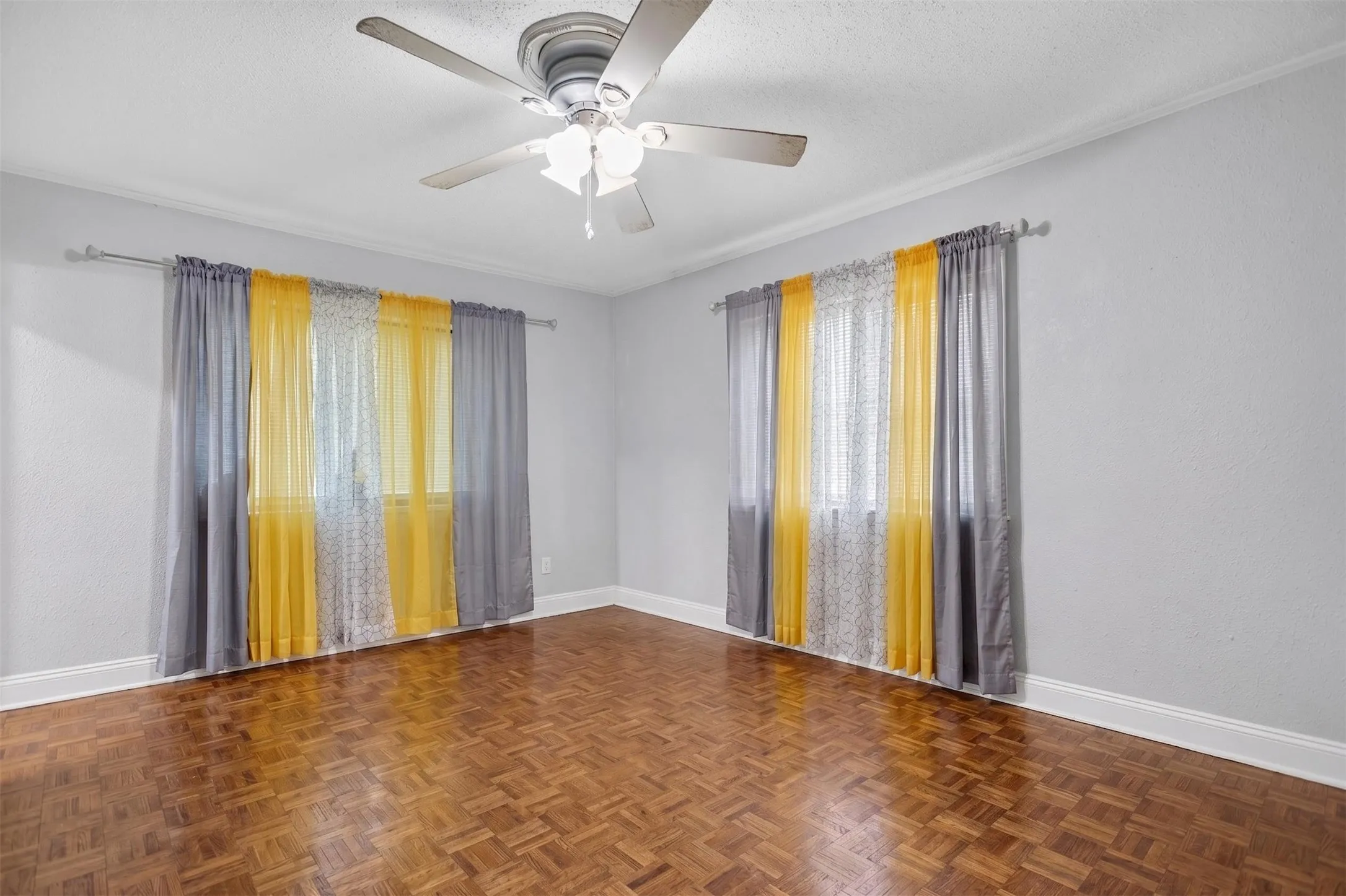 Room featuring parquet wood flooring, white baseboards, crown molding, and a ceiling fan with light fixture