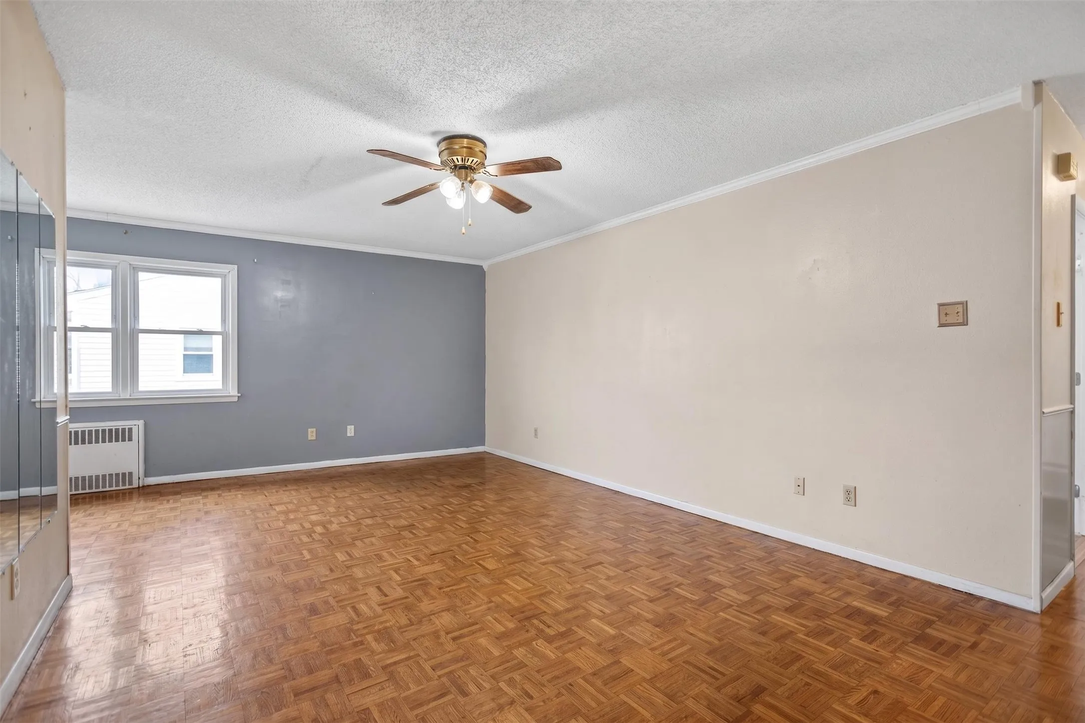 Spacious room featuring parquet wood flooring, a ceiling fan with integrated lighting, and a dual-pane window