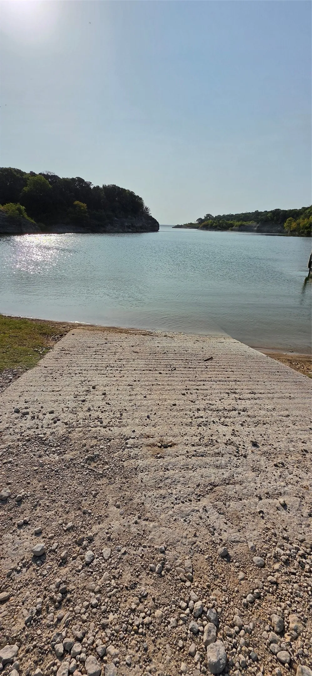 Concrete boat ramp leading to a body of water with tree-lined banks