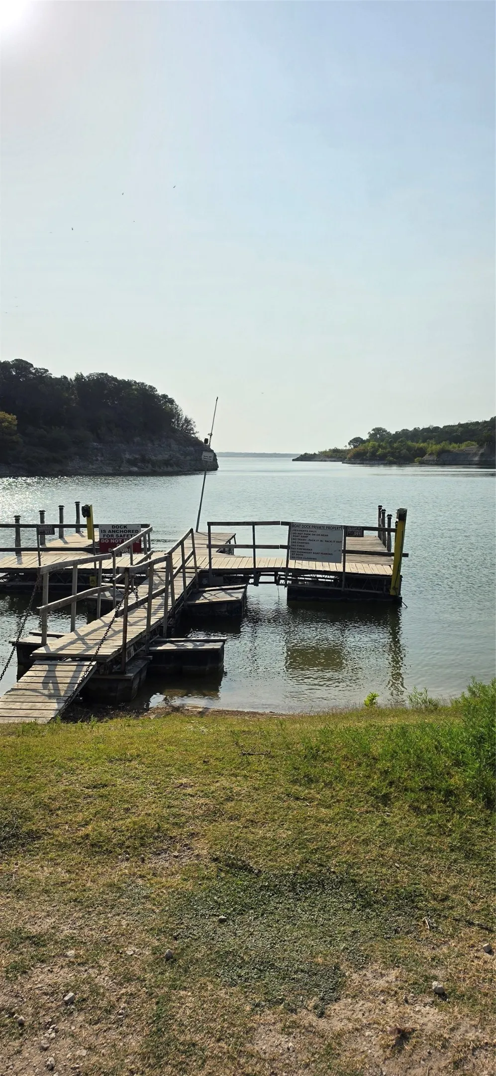 Wood-plank boat dock with handrails, situated on a calm body of water with a natural shoreline