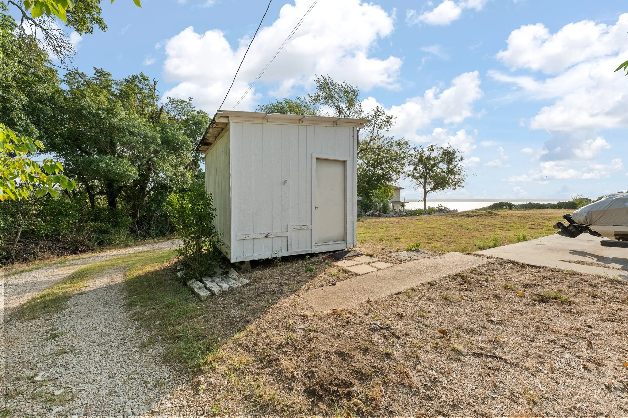 Utility structure featuring corrugated metal siding and a single entry door, situated on a spacious rural lot with mature trees and open grounds