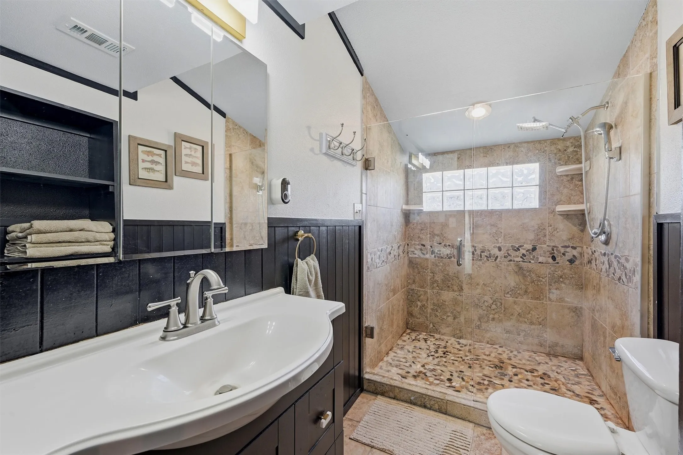 Tiled shower with glass enclosure, pebble floor, and built-in shelving