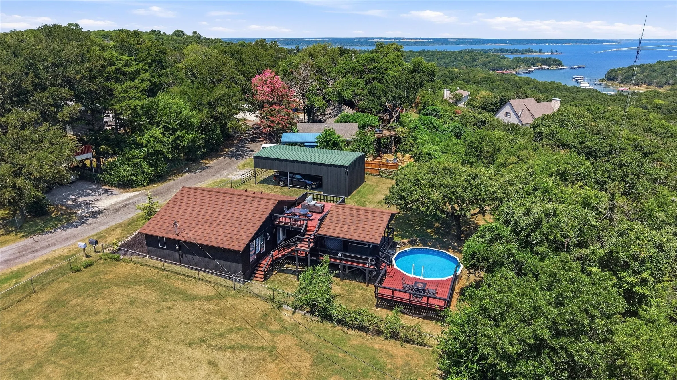Expansive property featuring a residence with a brown shingle roof, an elevated wood deck, and an above-ground pool
