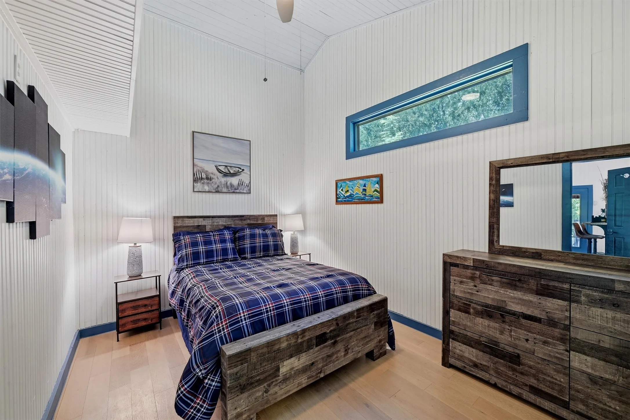 Vaulted ceiling with a ceiling fan, light wood-finish flooring, beadboard wall paneling, and a high horizontal window with blue trim