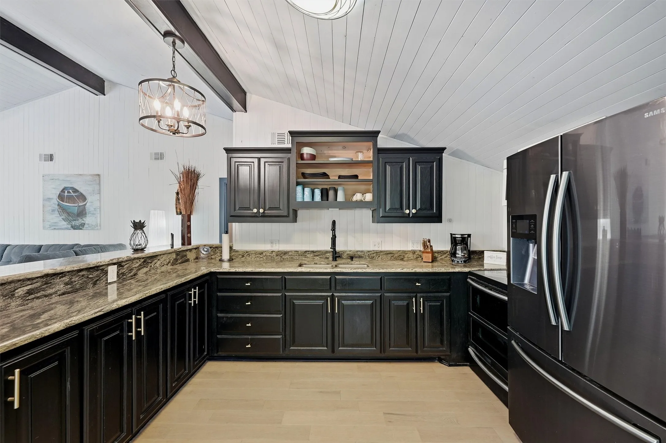 Kitchen featuring dark wood cabinetry, light wood-finish flooring, stone countertops, and a modern stainless steel refrigerator