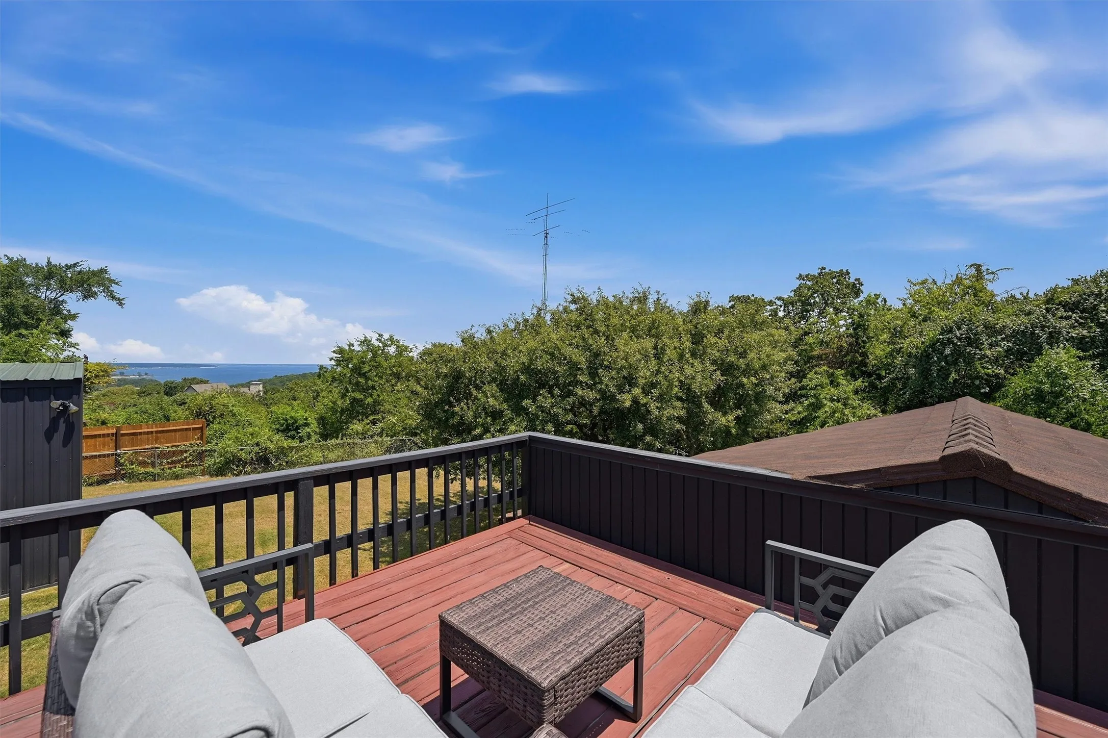 Expansive wood deck with a dark wood railing overlooking a distant body of water