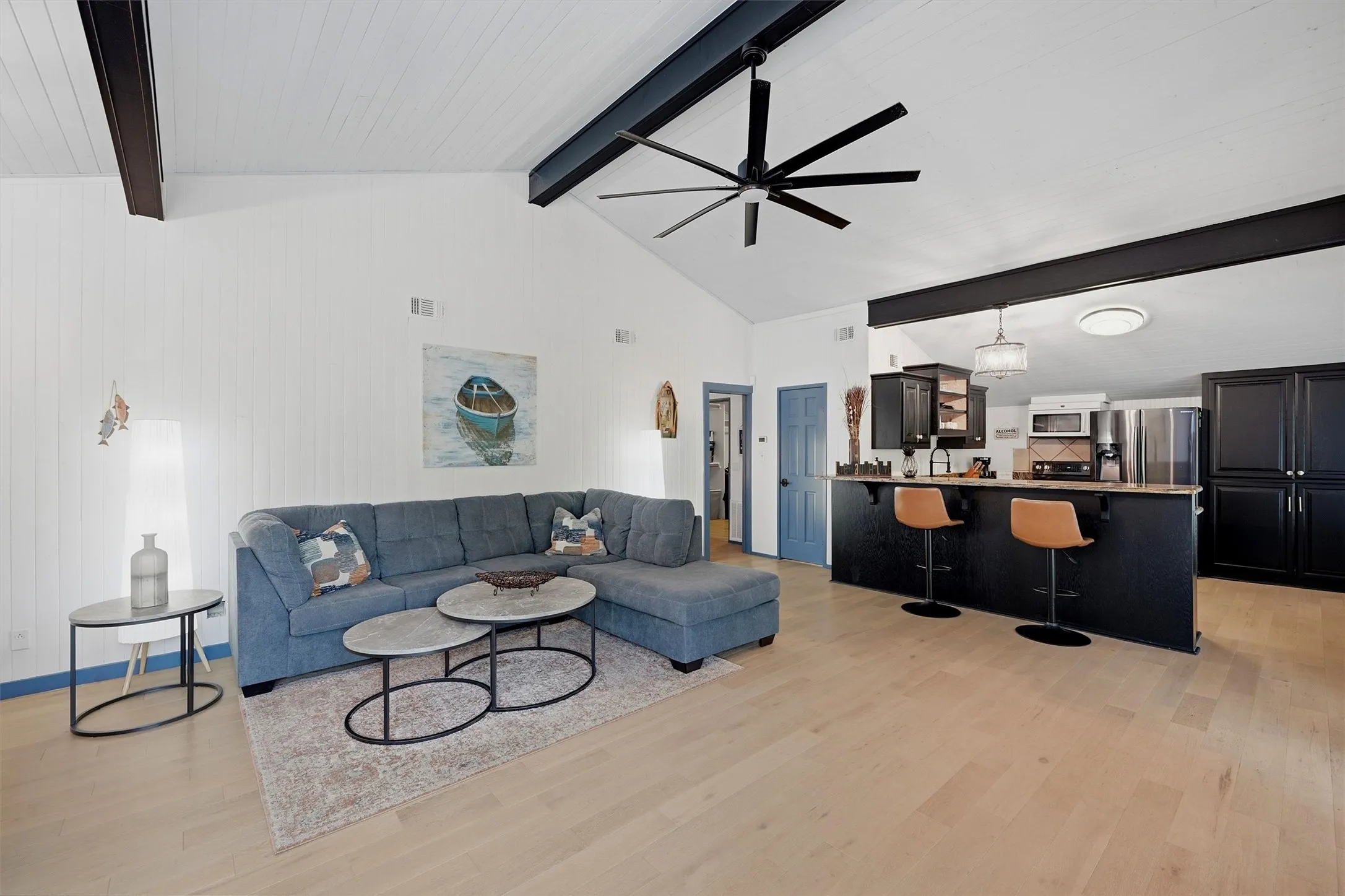 Vaulted ceiling with exposed beams, light wood-finish flooring, kitchen island with counter seating, built-in cabinetry, and a ceiling fan