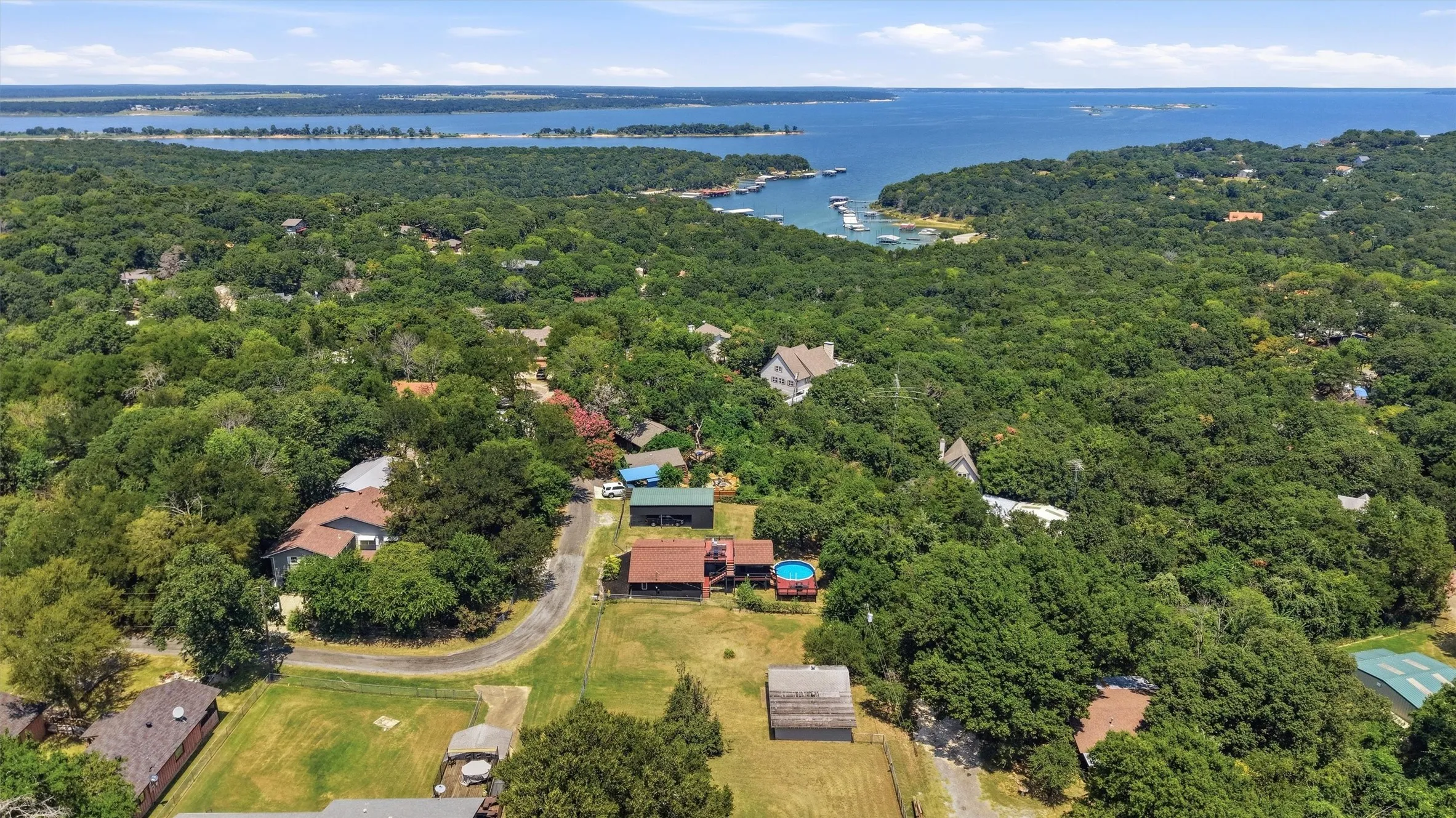 Expansive property featuring a curved asphalt driveway, mature trees, an above-ground pool, and multiple outbuildings