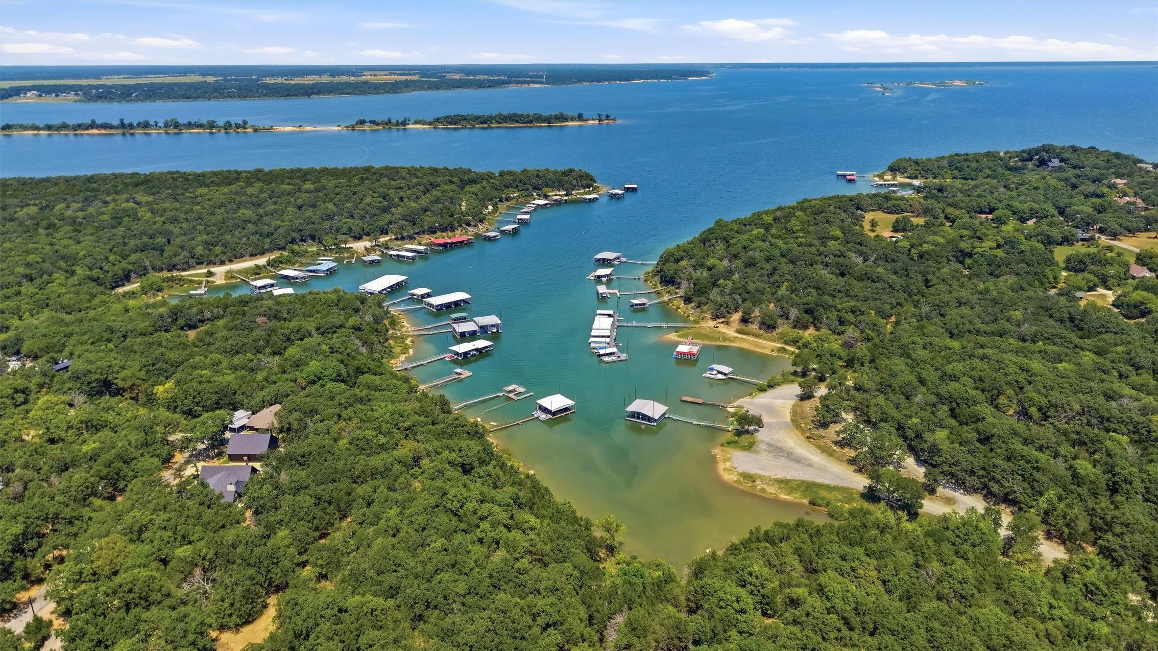 Waterfront property featuring extensive tree coverage and multiple boat docks along a cove leading to an expansive body of water