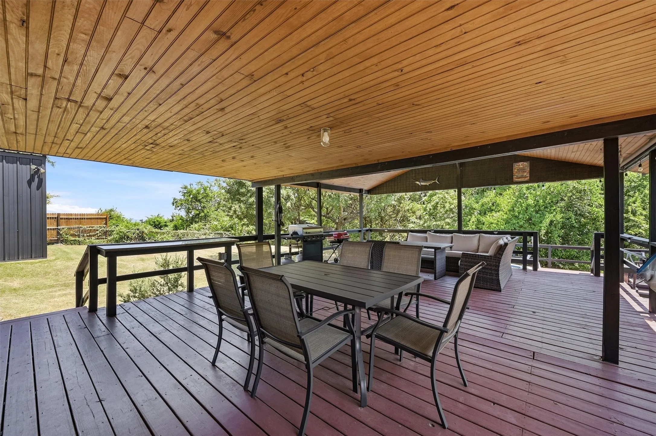 Expansive covered deck featuring a wood-plank ceiling, slatted decking, and sturdy railing