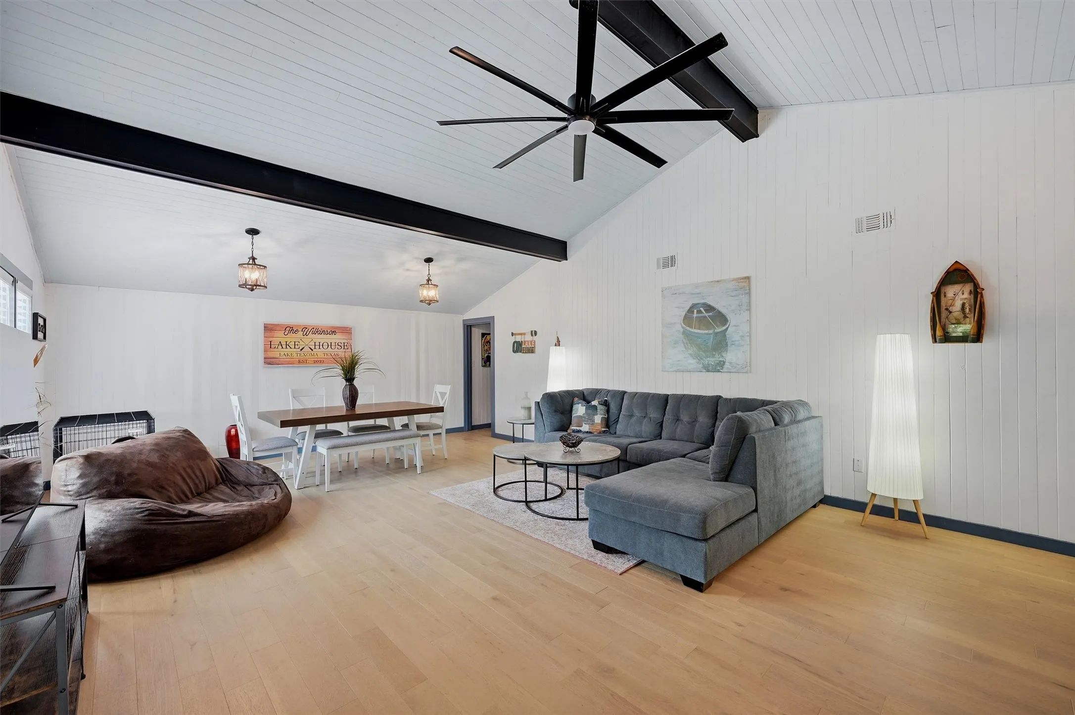 Vaulted ceiling with exposed beams, wood-finish flooring, white vertical wall paneling, and two pendant light fixtures