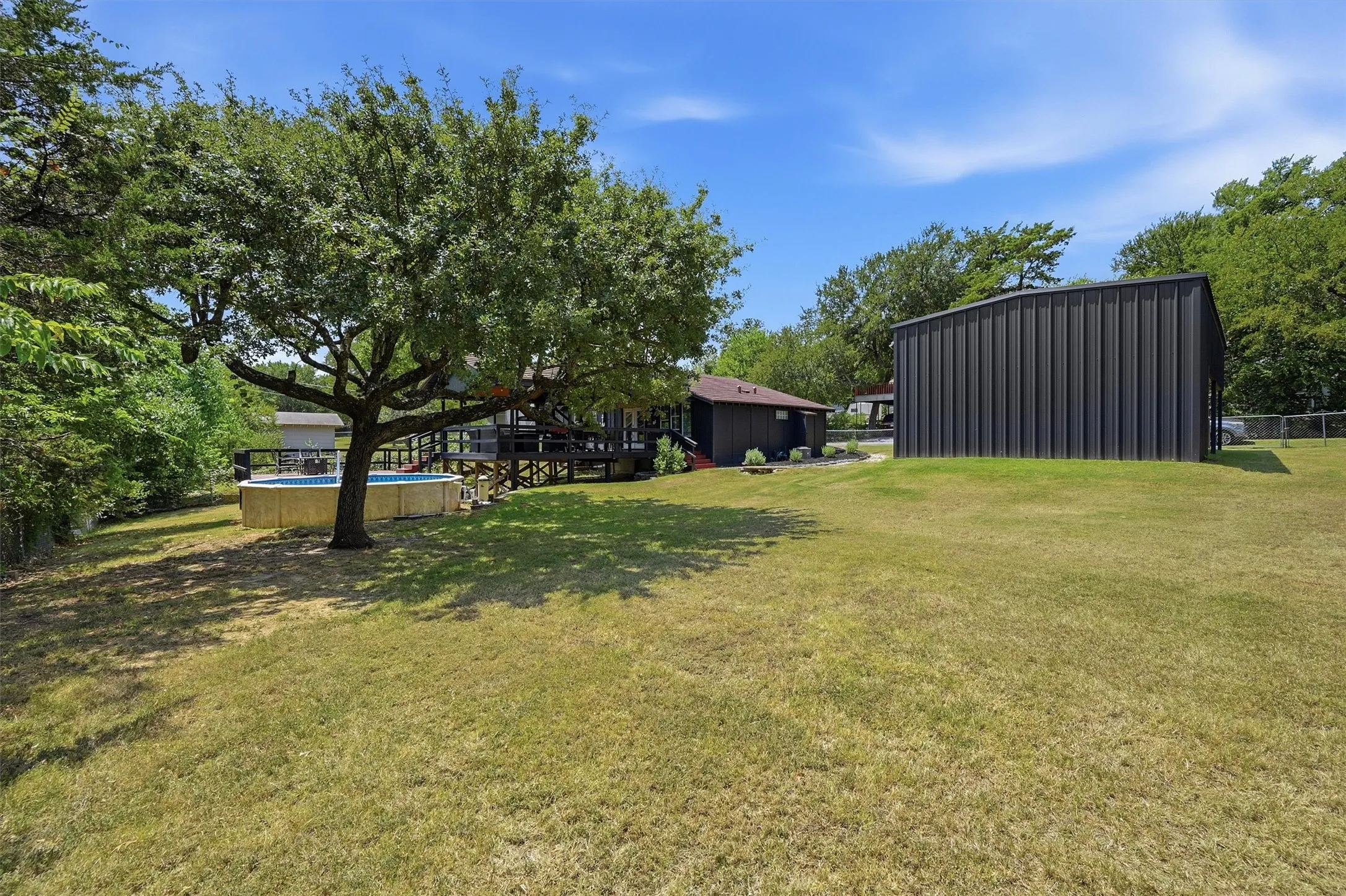 Expansive lawn featuring mature trees, an above-ground pool, and a dark-paneled auxiliary building
