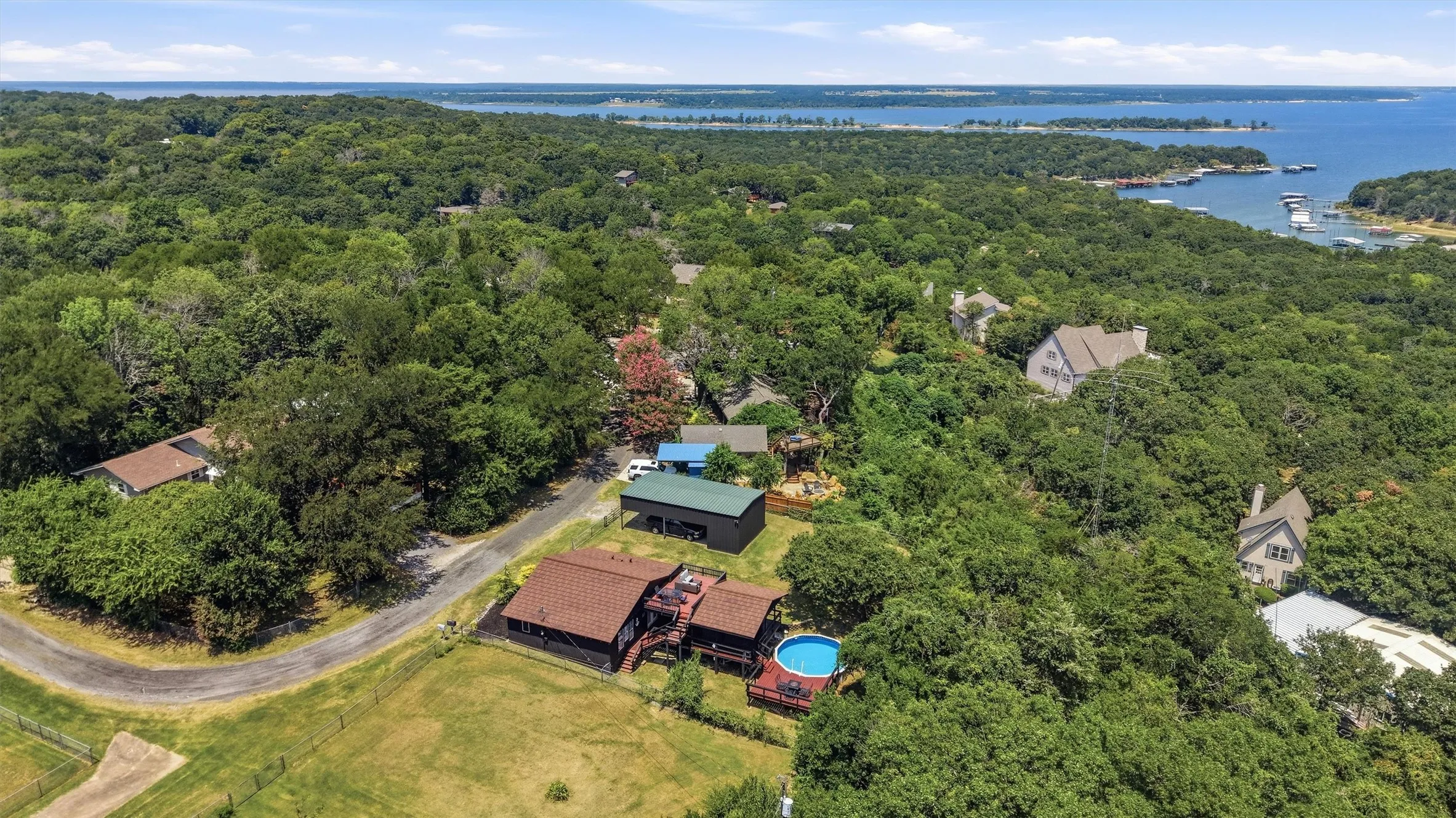 Property situated amidst dense mature trees with an above-ground pool, expansive deck, and distant water body