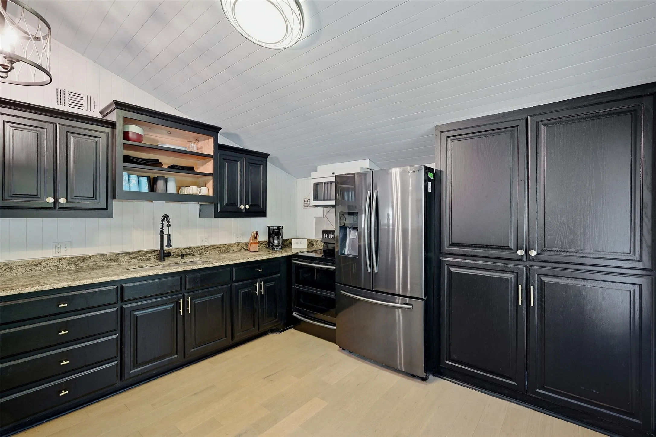 Kitchen featuring dark cabinetry, light wood-finish flooring, a stone-finish countertop, and stainless steel appliances