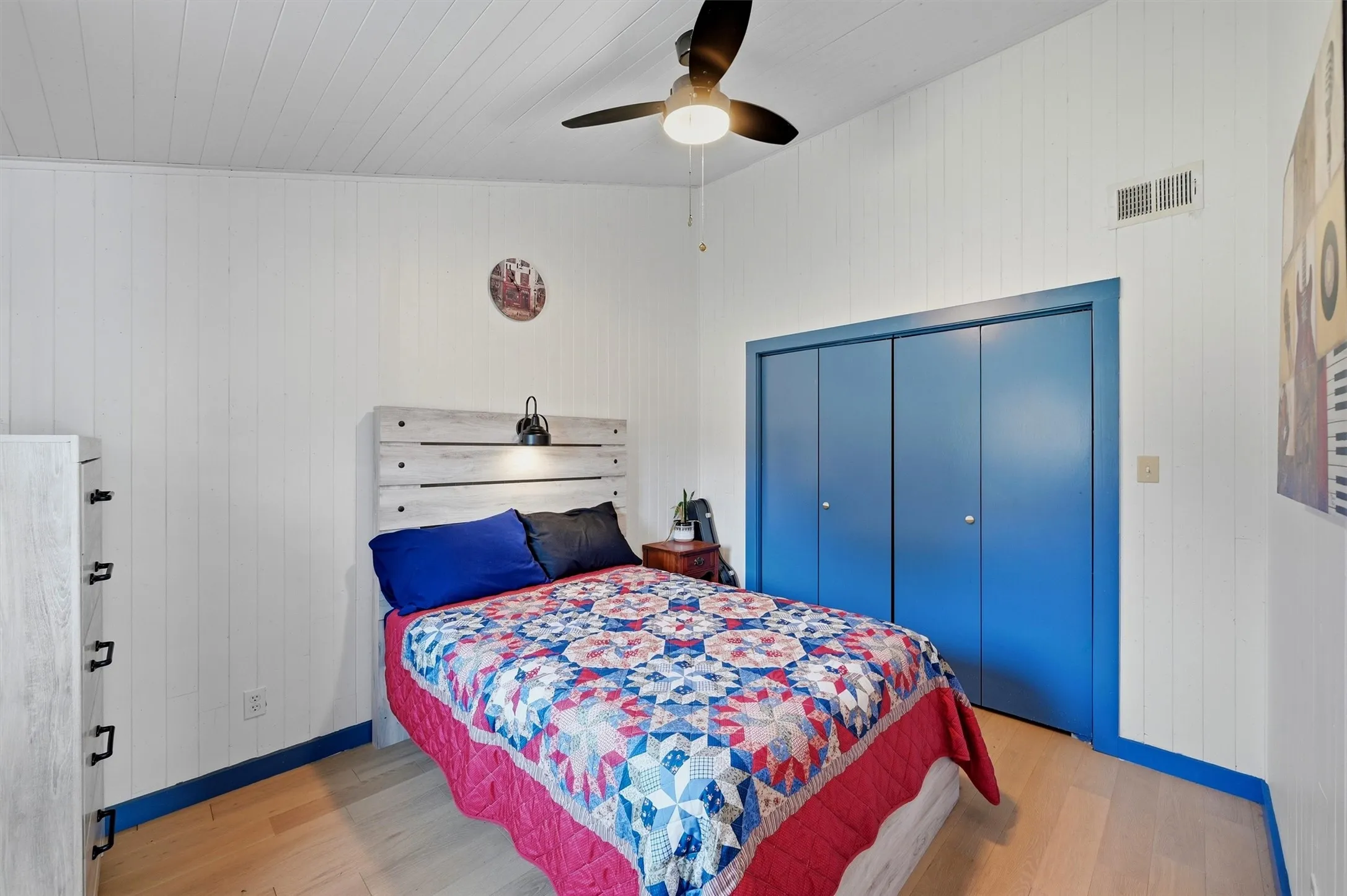 Wood-finish flooring, white paneled walls, and a white paneled ceiling with a dark-toned ceiling fan