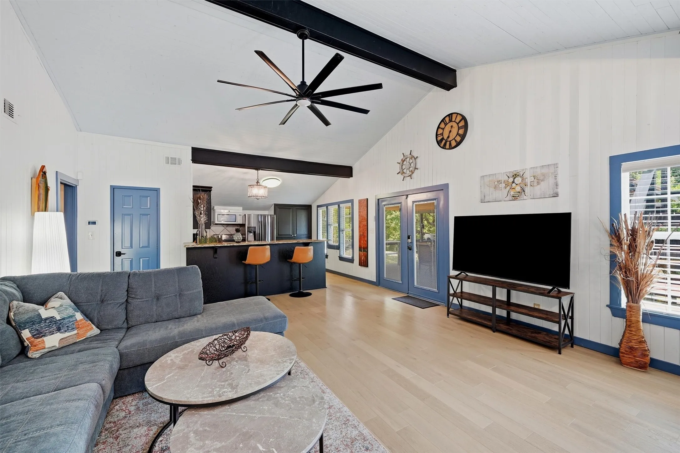 Vaulted ceiling with exposed beams, wood-finish flooring, kitchen with breakfast bar, blue-trimmed windows and doors, and a ceiling fan