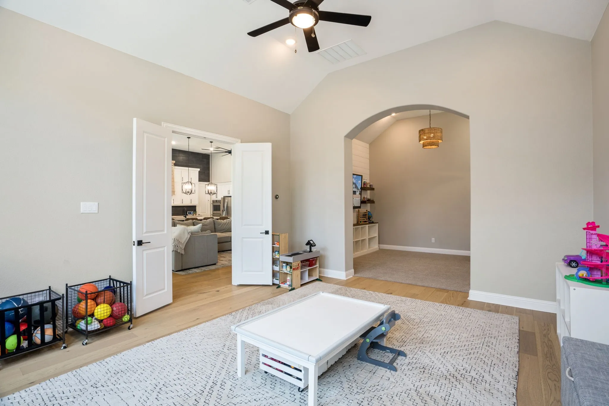 Spacious recreation room featuring soaring vaulted ceilings with ceiling fan, arched architectural alcove with pendant lighting and built-in shelving, hardwood-finish flooring throughout, and multiple entry points including French doors to adjacent spaces