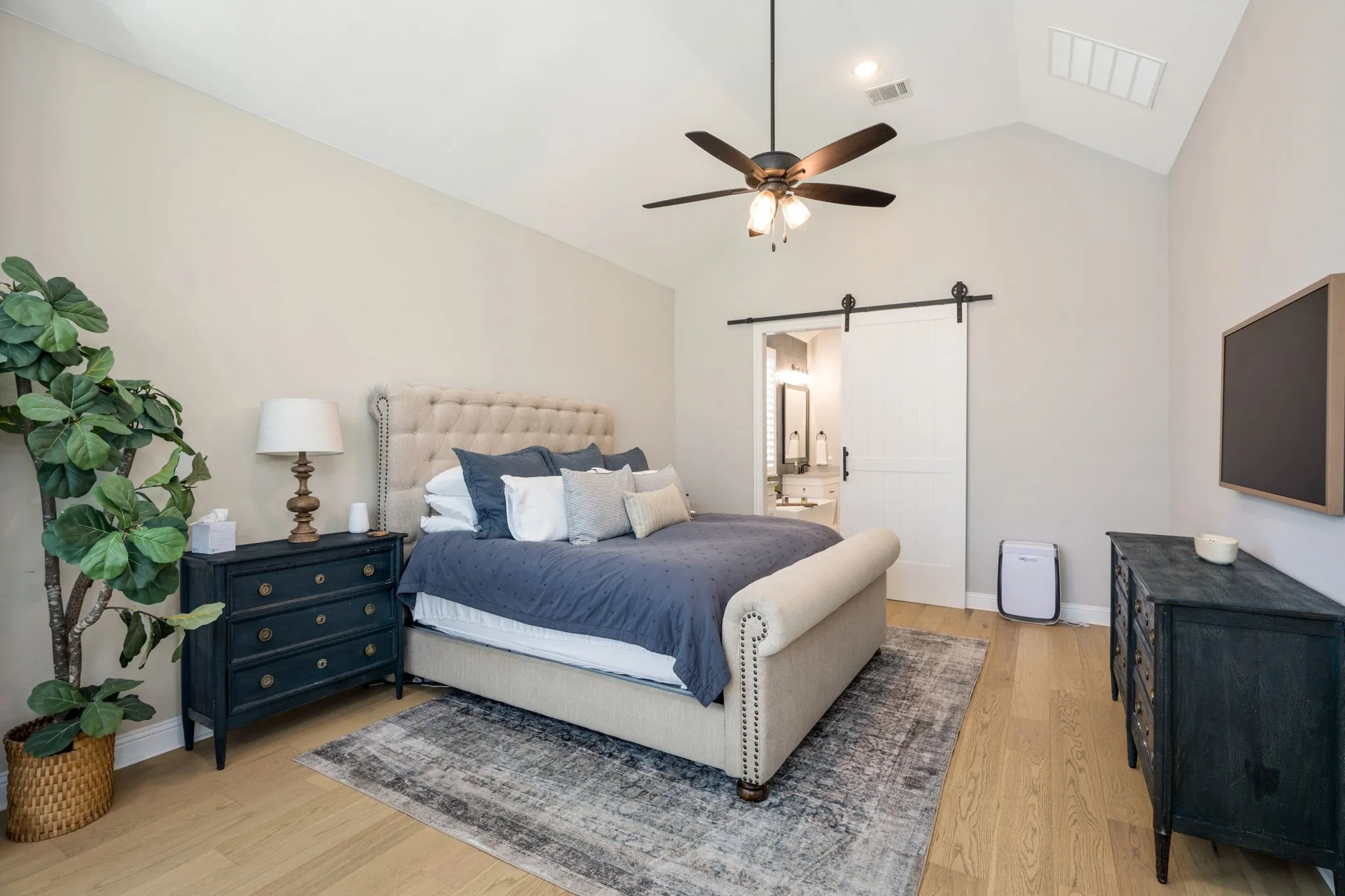 Spacious primary bedroom featuring vaulted ceilings with skylights, a ceiling fan with integrated lighting, and wood-finish flooring throughout
