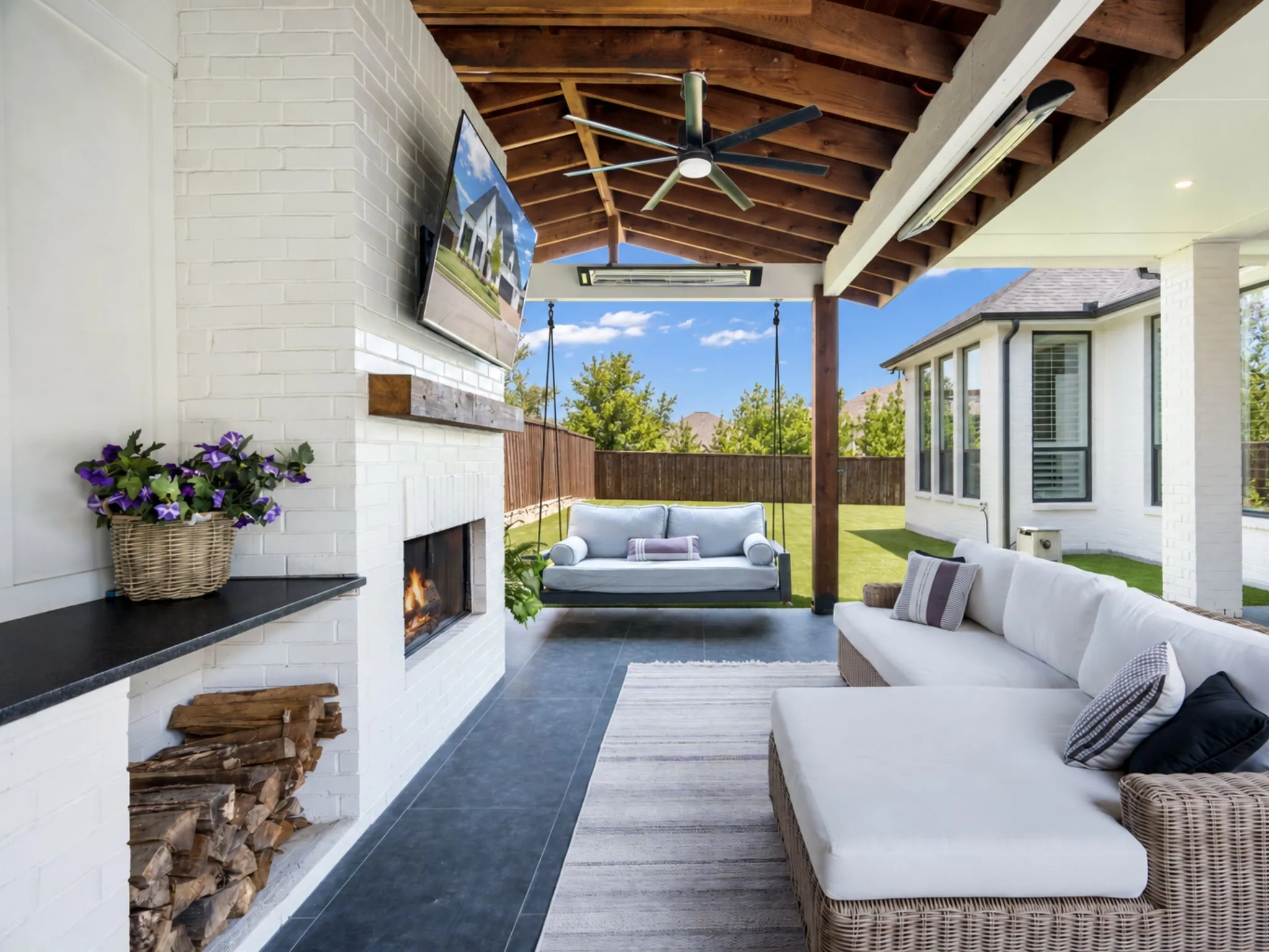 Covered outdoor patio featuring a painted brick fireplace, wood-beam ceiling, ceiling fan, and tile flooring