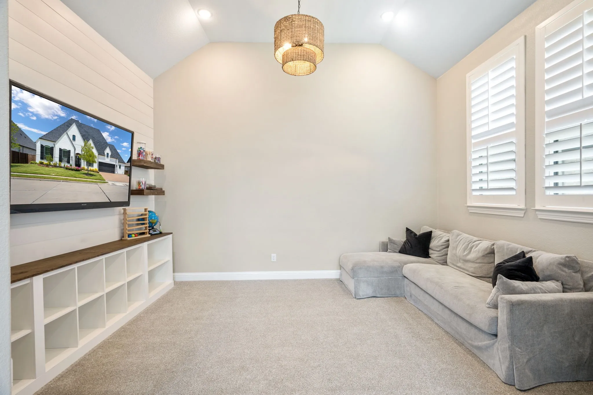 Vaulted ceiling room featuring a shiplap accent wall, built-in shelving with wood-finish countertop, plantation shutters, recessed lighting, and a tiered pendant fixture
