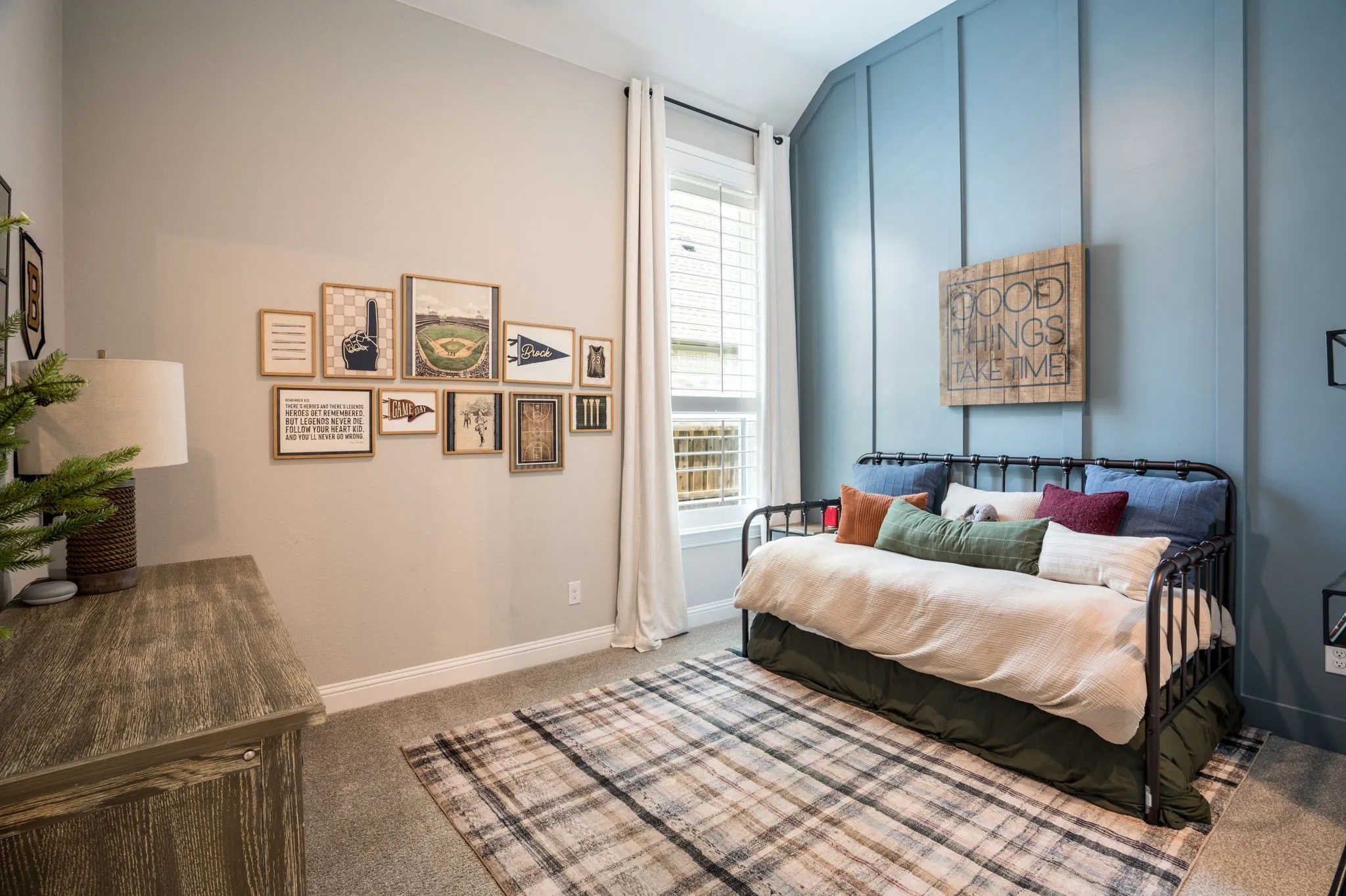 Bedroom featuring floor-to-wall blue accent walls, a black metal bed frame with cream bedding, wood-finish flooring, a plaid area rug, and curated gallery wall art