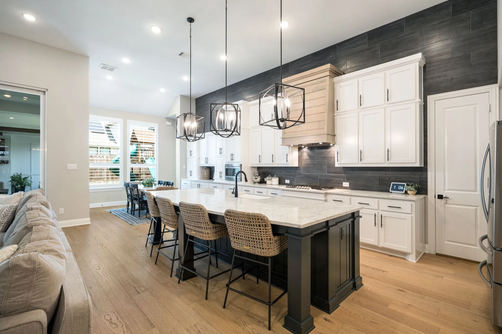 Kitchen featuring a large central island with seating, pendant lighting, white cabinetry, dark full-height backsplash, and light wood-finish flooring