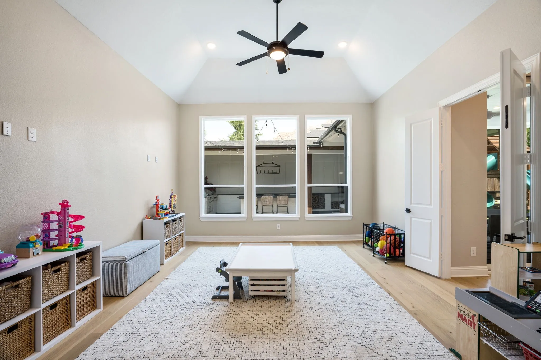 Bright, airy playroom showcasing soaring vaulted ceilings, a ceiling fan with integrated lighting, and abundant natural light from triple casement windows