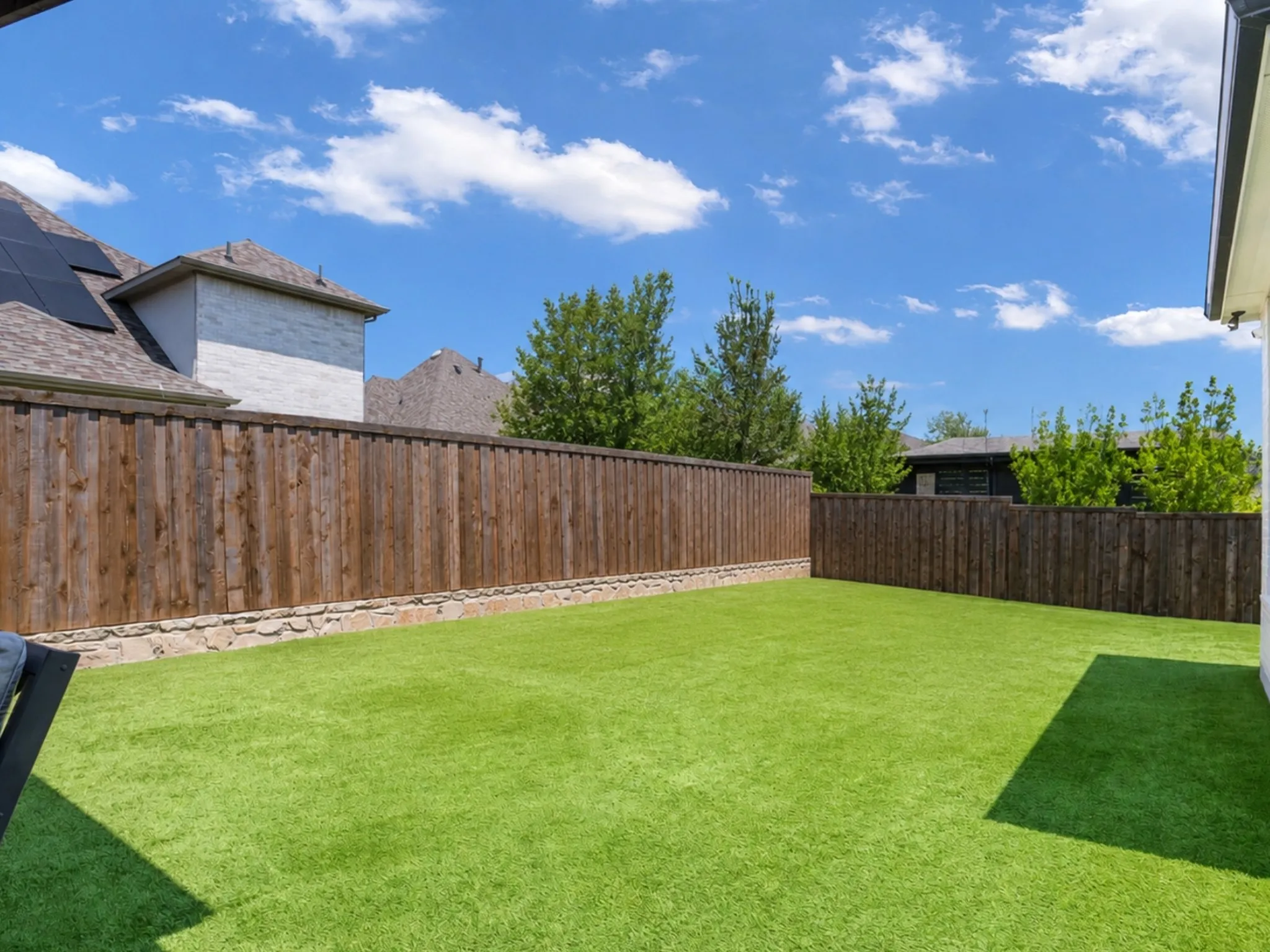 Backyard featuring synthetic turf, perimeter wood fencing, and a natural stone retaining wall