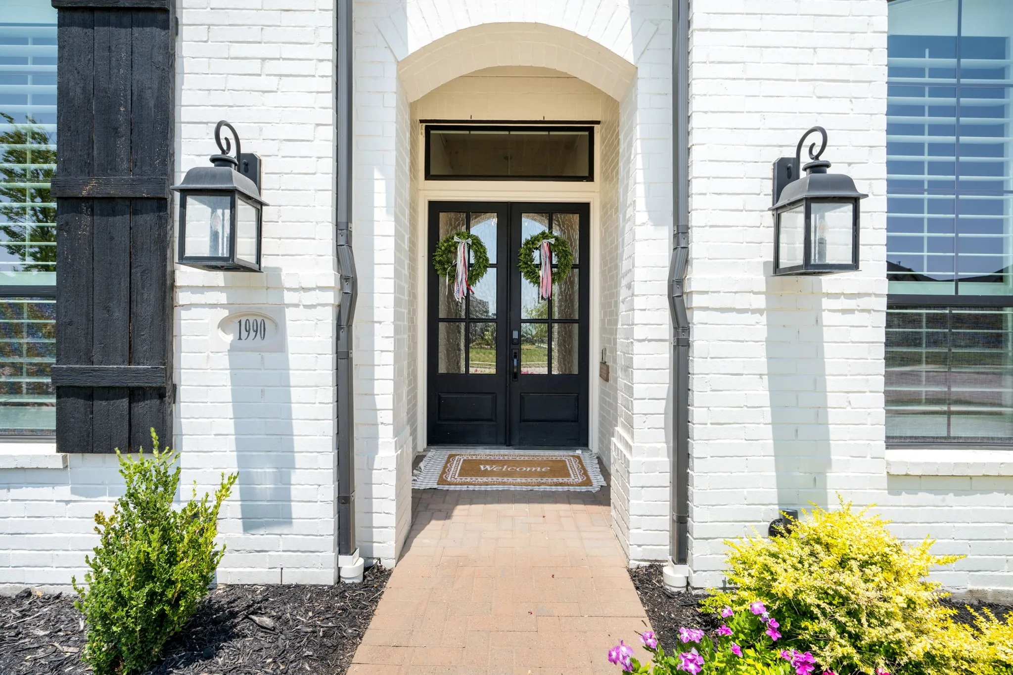 Arched entry featuring a black paneled door with glass inserts, flanked by decorative outdoor lanterns